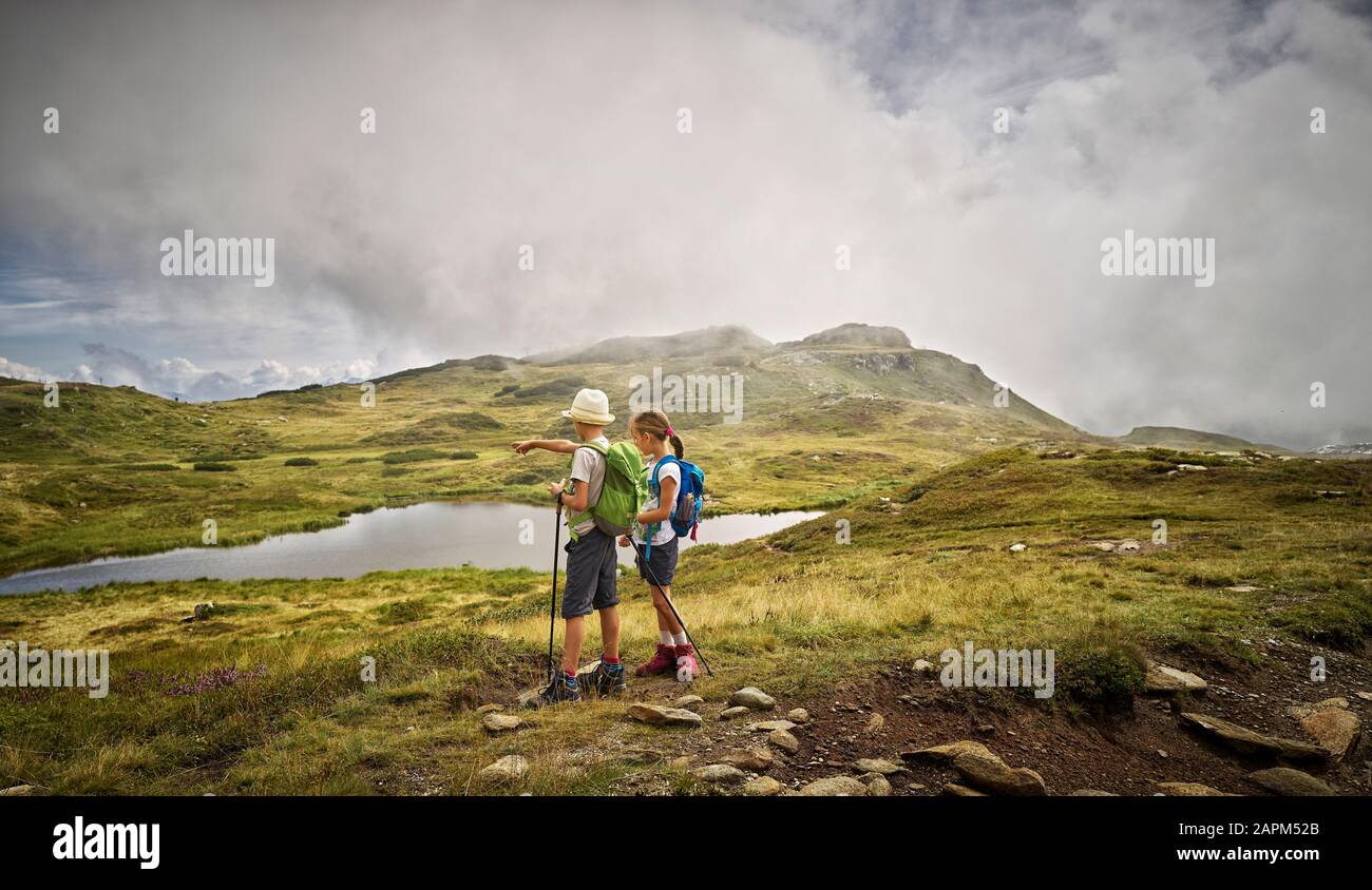 Ragazzo e ragazza in piedi in un lago in paesaggio alpino, Val Passiria, Alto Adige, Italia Foto Stock