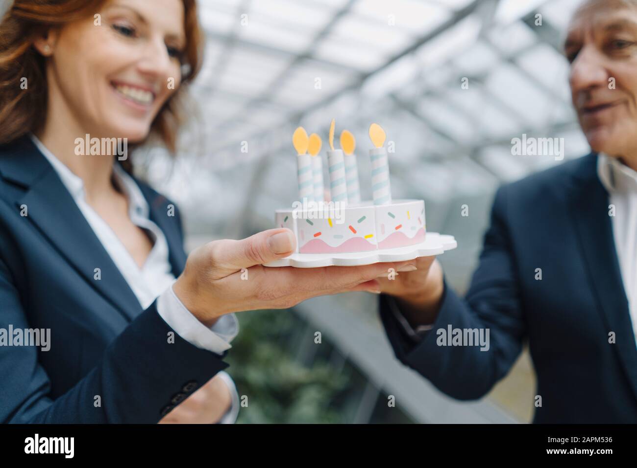 Uomo d'affari e donna d'affari che festeggiano il compleanno in ufficio con la torta di compleanno falsa Foto Stock