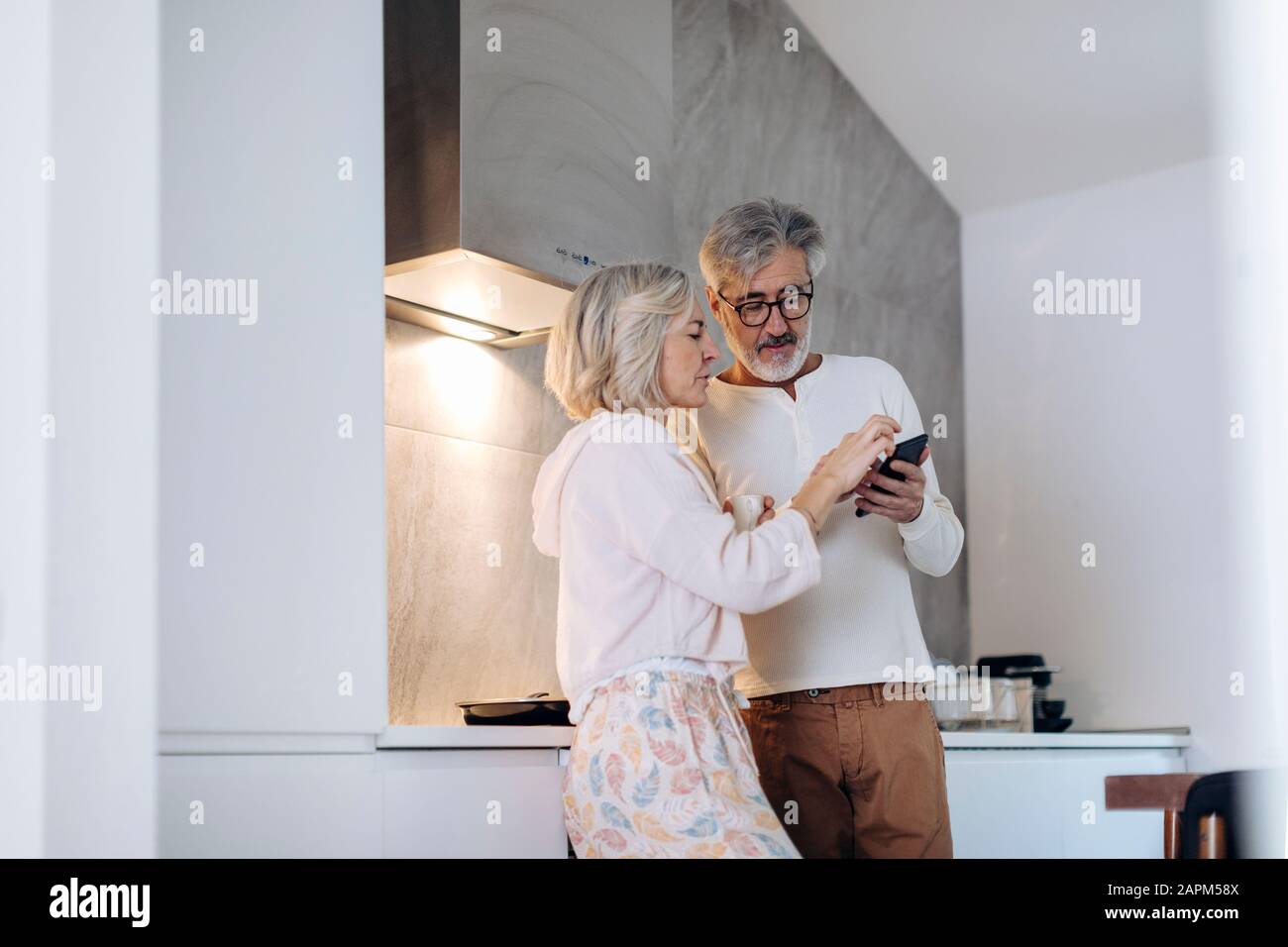 Coppia matura utilizzando cellulare in cucina a casa Foto Stock