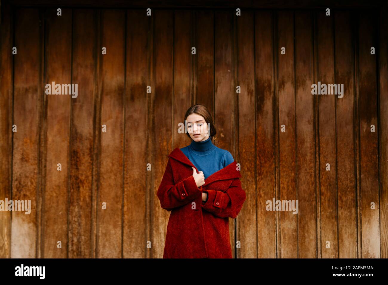 Primo piano ritratto di donna con turtleneck blu pullover e cappotto rosso di fronte a una porta di legno Foto Stock