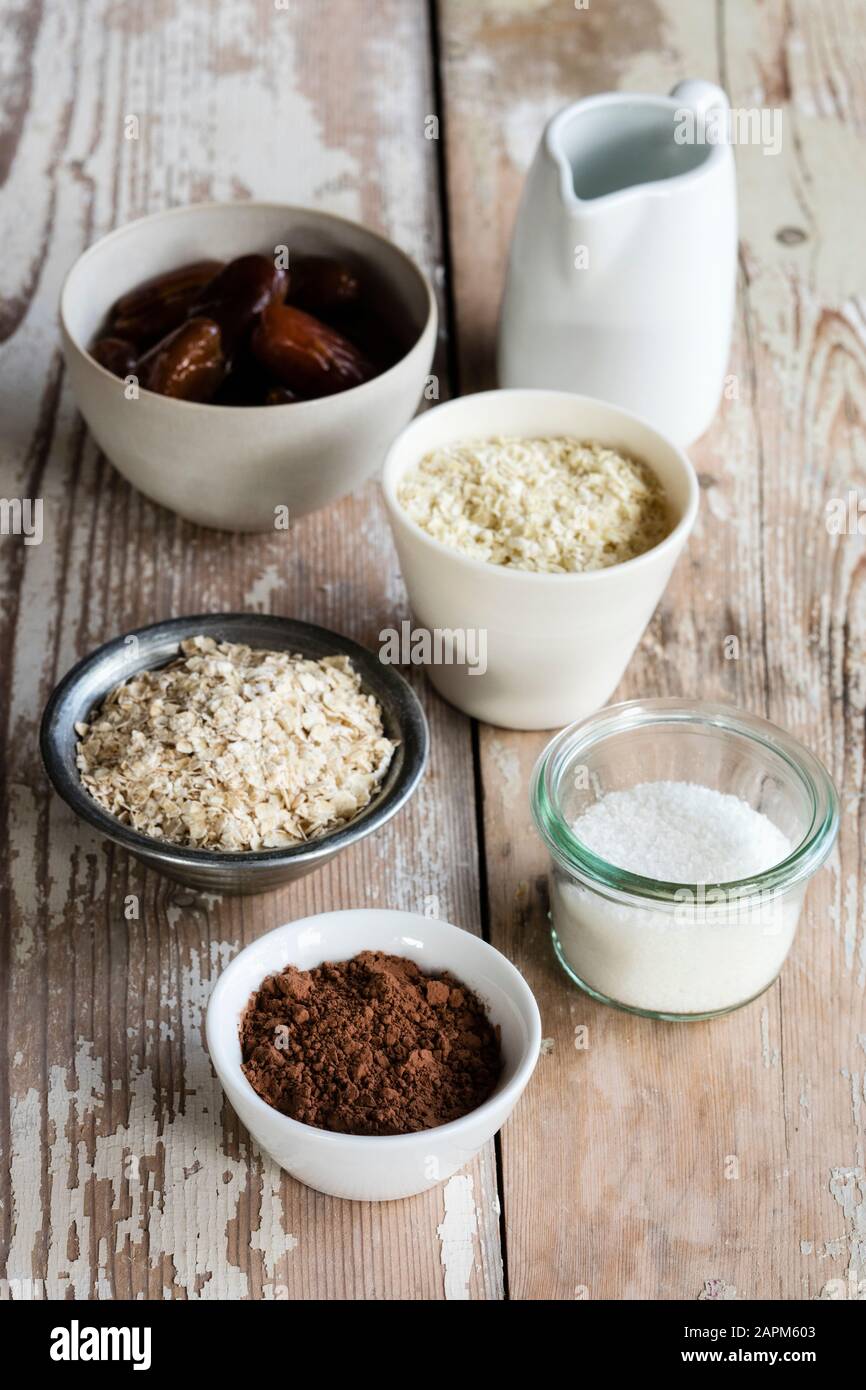 Ingredienti per la preparazione di palle proteiche (olio di cocco, datteri, fiocchi di miglio, fiocchi di avena, cocco grattugiato e polvere di cacao) Foto Stock