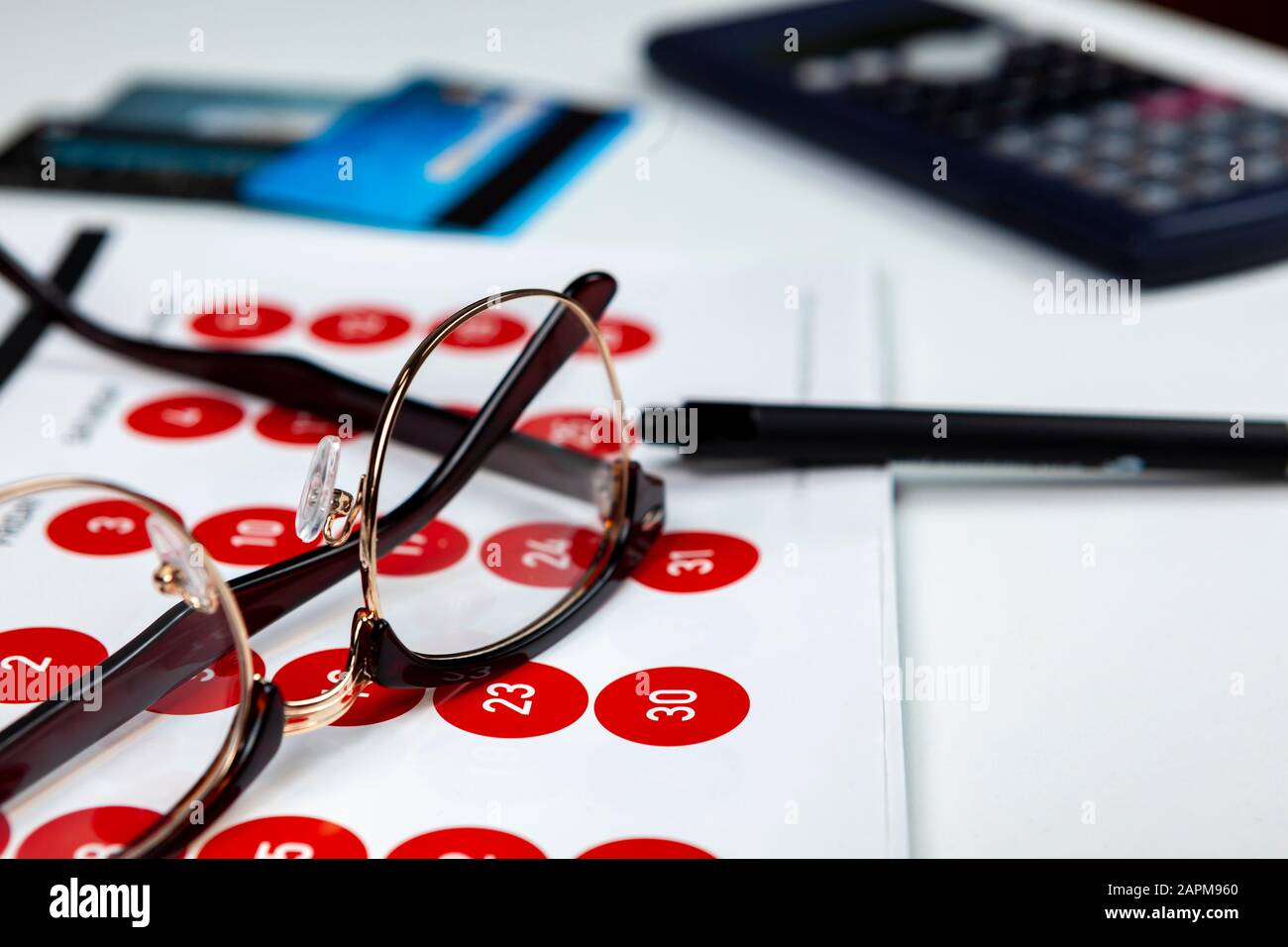 Un paio di occhiali neri a montatura che si posano su un calendario con alcune carte di credito accanto a una calcolatrice Foto Stock