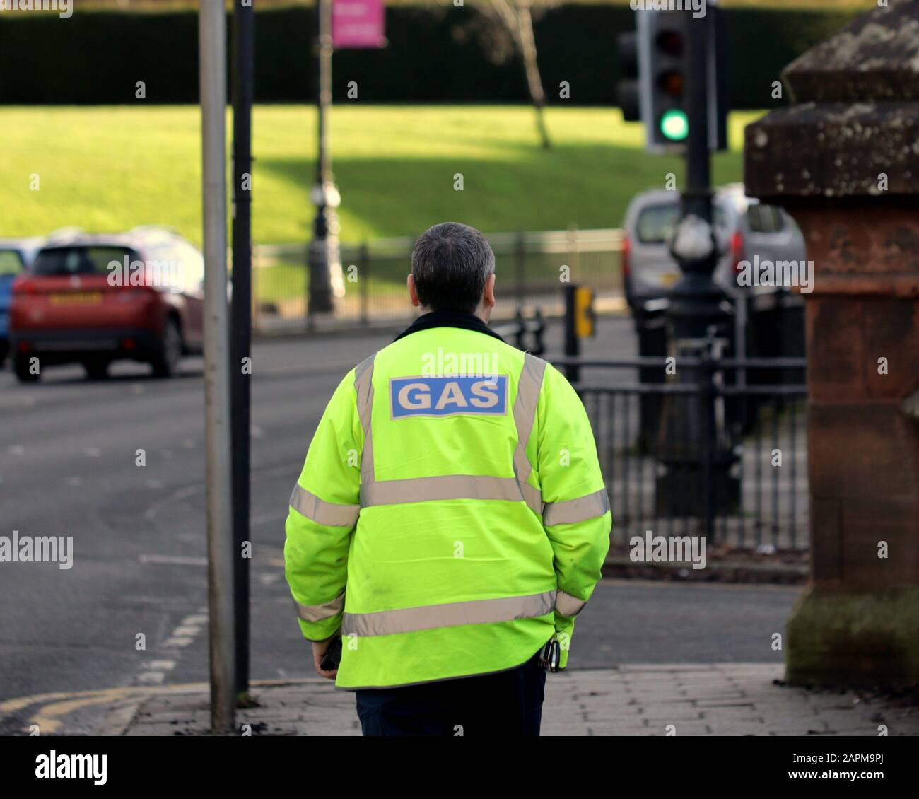Lavoratore a gas in giubbotto ad alta visibilità a piedi sulla strada visto da dietro Foto Stock