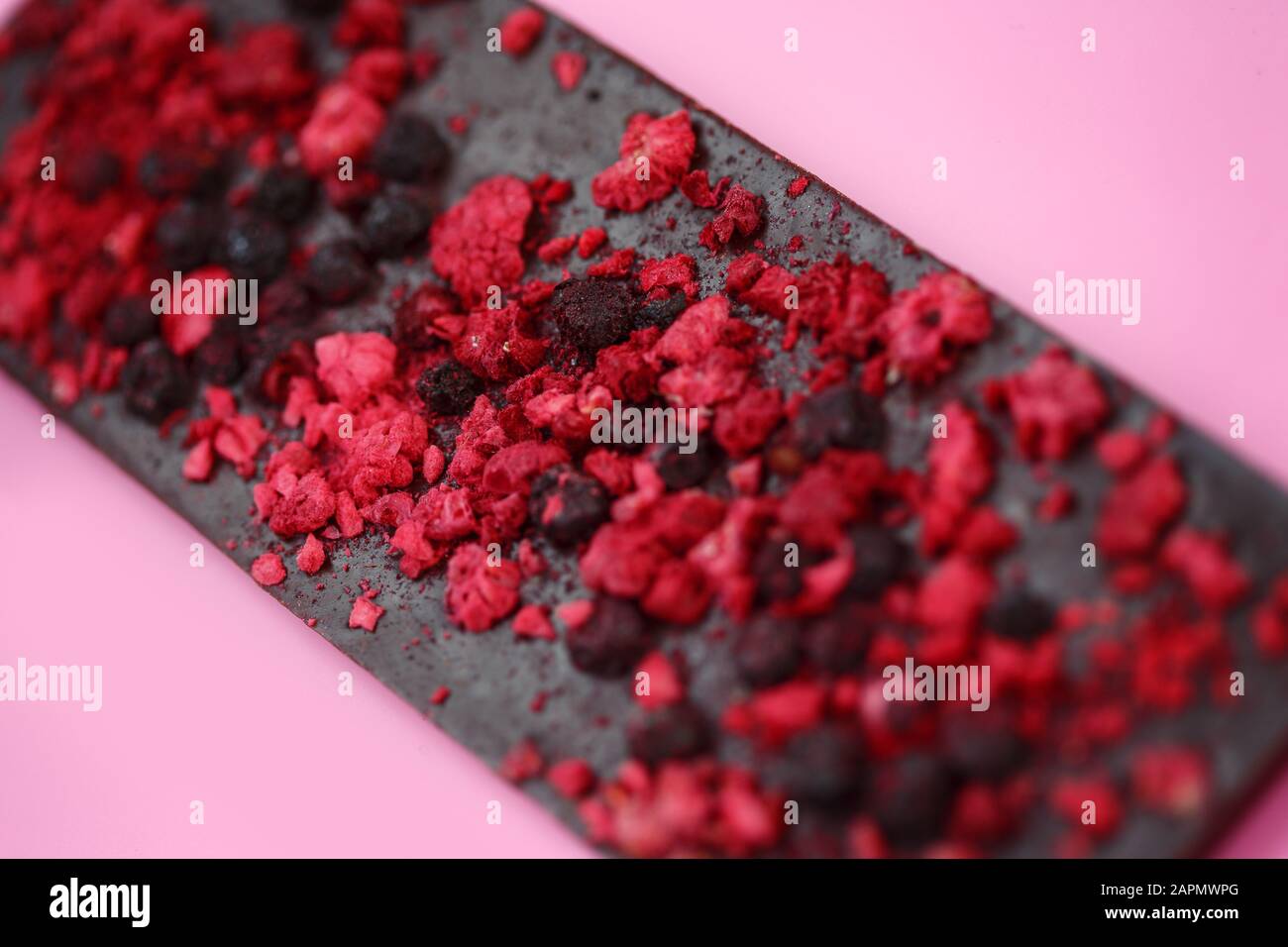 Cioccolato a basso contenuto calorico nero con frutti di bosco rossi secchi su sfondo rosa brillante, fuoco selettivo Foto Stock