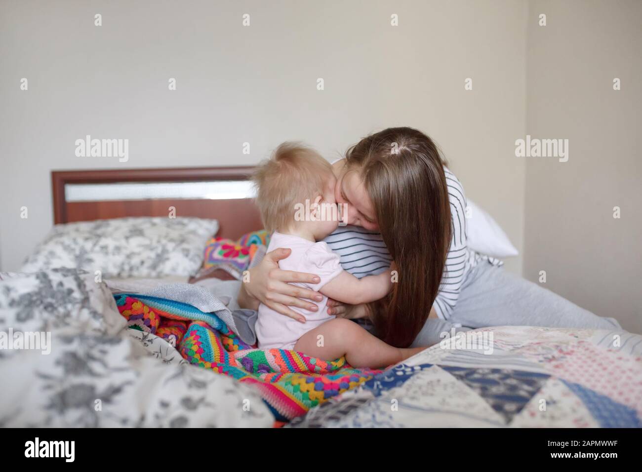 Bella madre giovane abbracciando e confortando il suo bambino piccolo neonato su un letto in camera da letto nel tempo di mattina Foto Stock