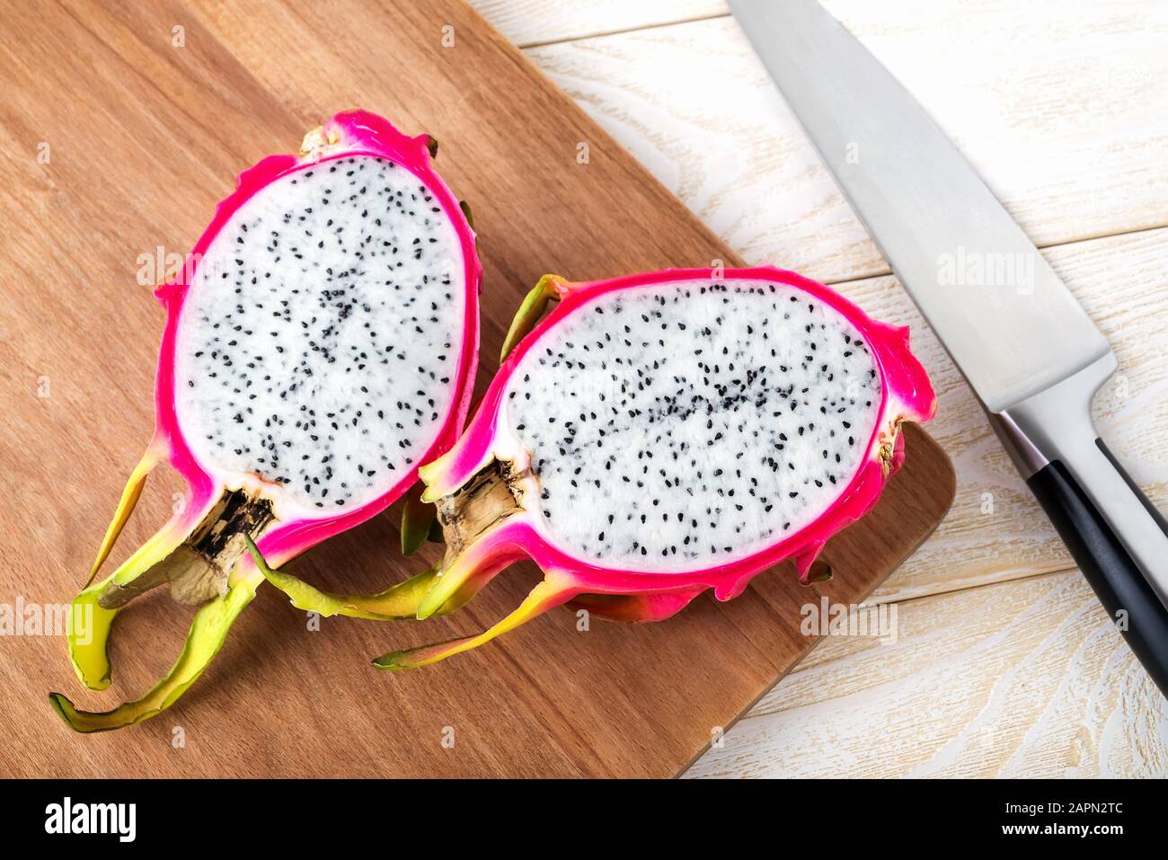 Frutti di drago maturi o pitaya tagliati a metà su una tavola di cotenna di legno marrone vicino a coltello affilato. Sano vegetariano ricco di vitamine B e tannino. Foto Stock