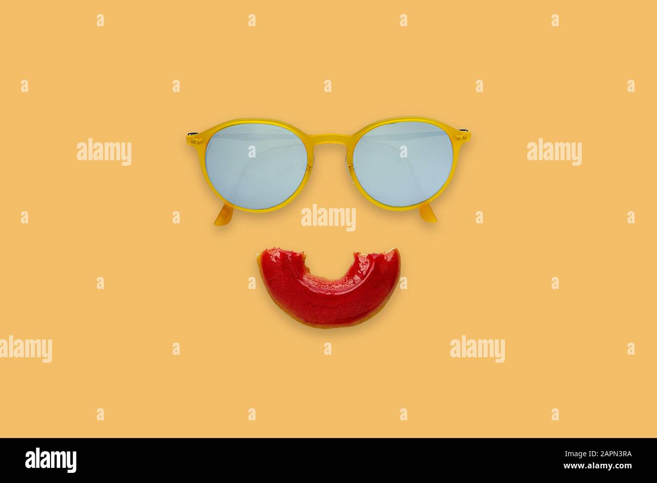 Occhiali da sole gialli e set di ciambelle rosse a metà bittente come bocca sorridente su sfondo arancione per un concetto minimo ed estivo. Foto Stock