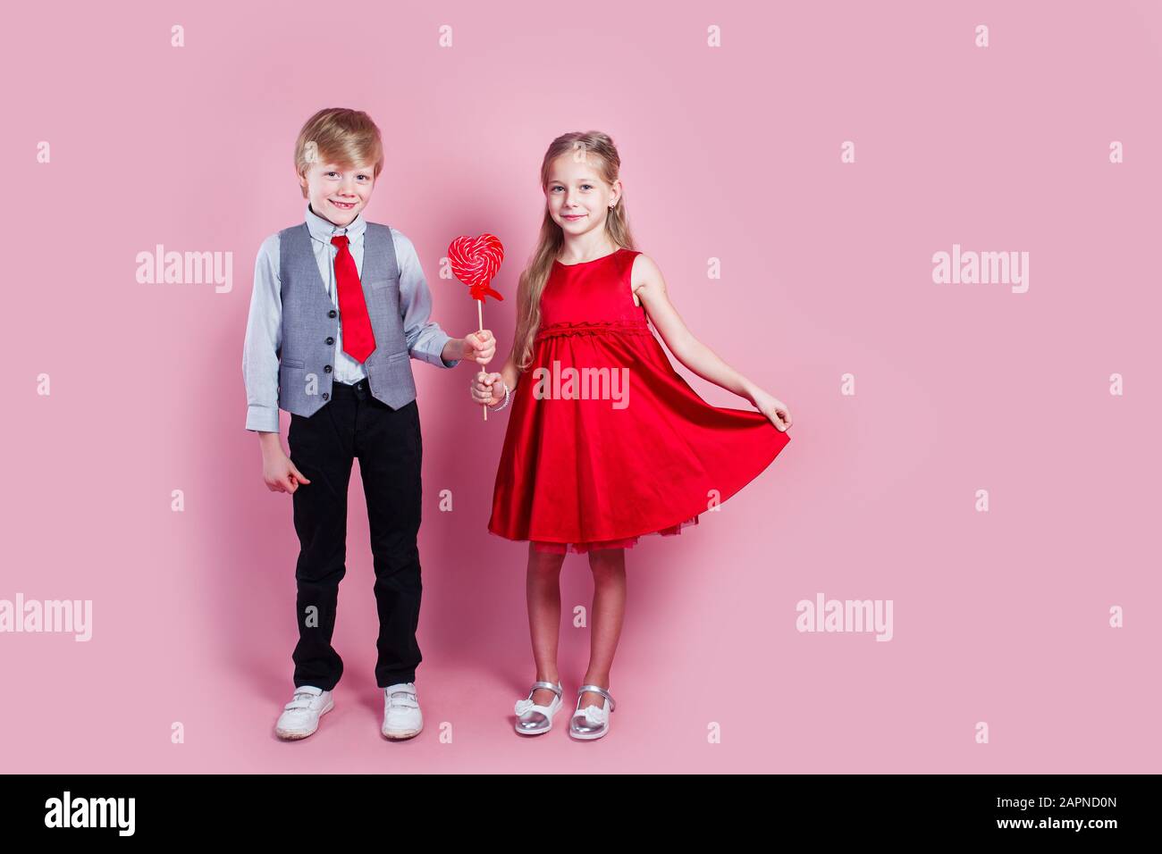 Ragazzo divertente e bambina con lecca pop rosso caramella in forma di cuore. Foto Stock