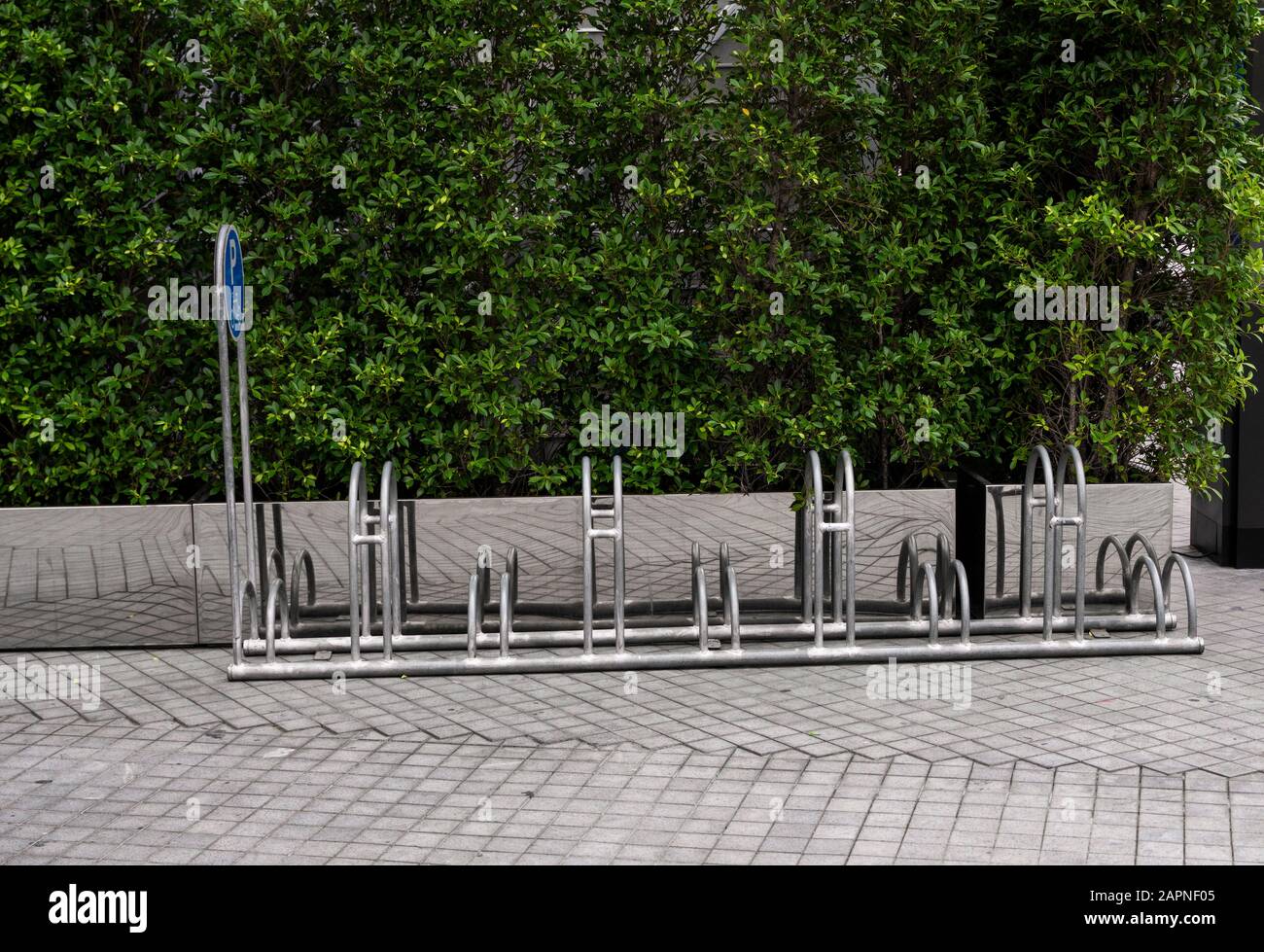 Vuoto in acciaio inossidabile parcheggio bici rack con un segno di parcheggio per le biciclette con un piante verdi su una parete. Foto Stock