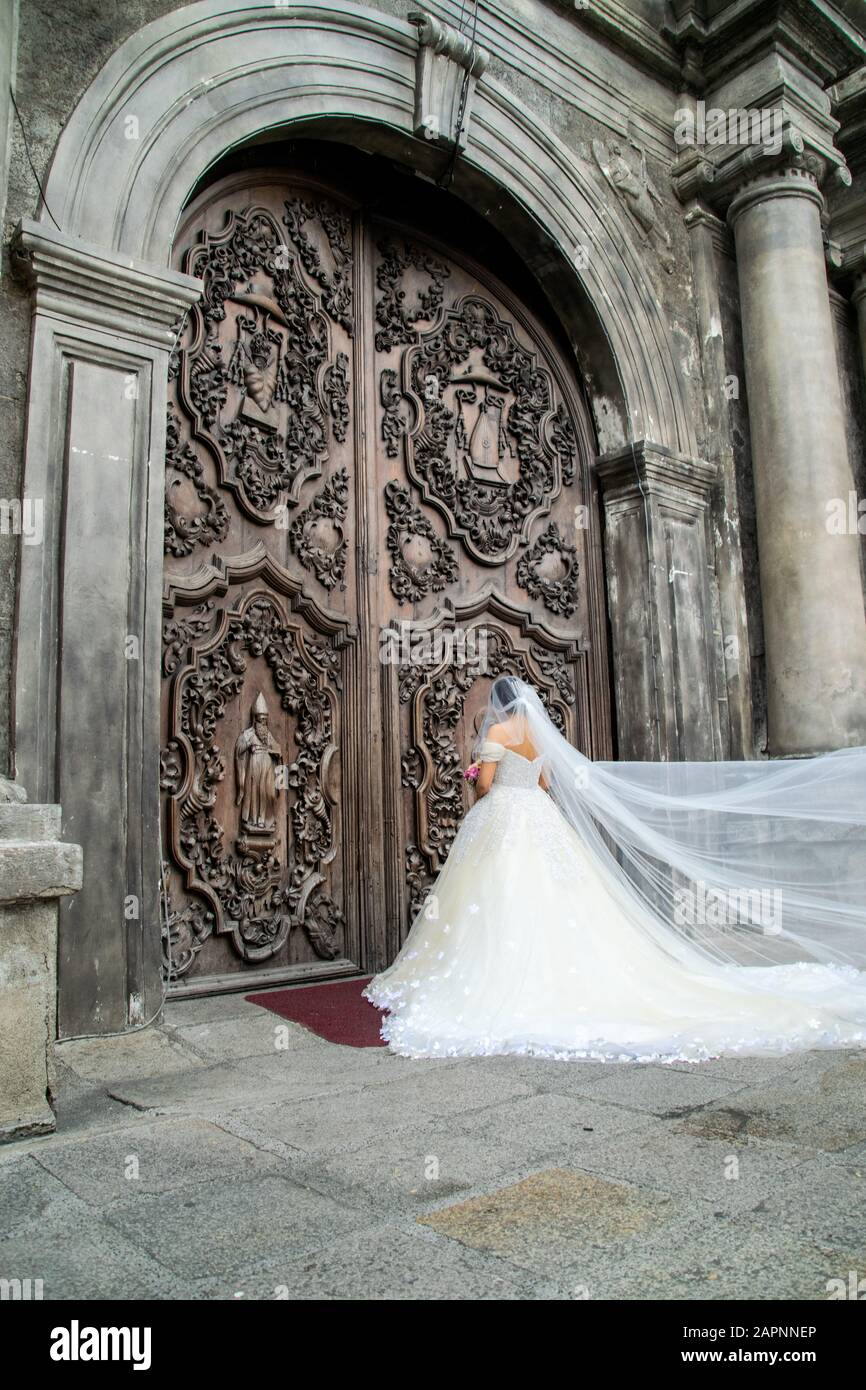 Sposa nel suo abito da sposa e velo fuori dalla Chiesa di San Agustin, di fronte alle porte della vecchia chiesa, in attesa che inizi la cerimonia nuziale Foto Stock