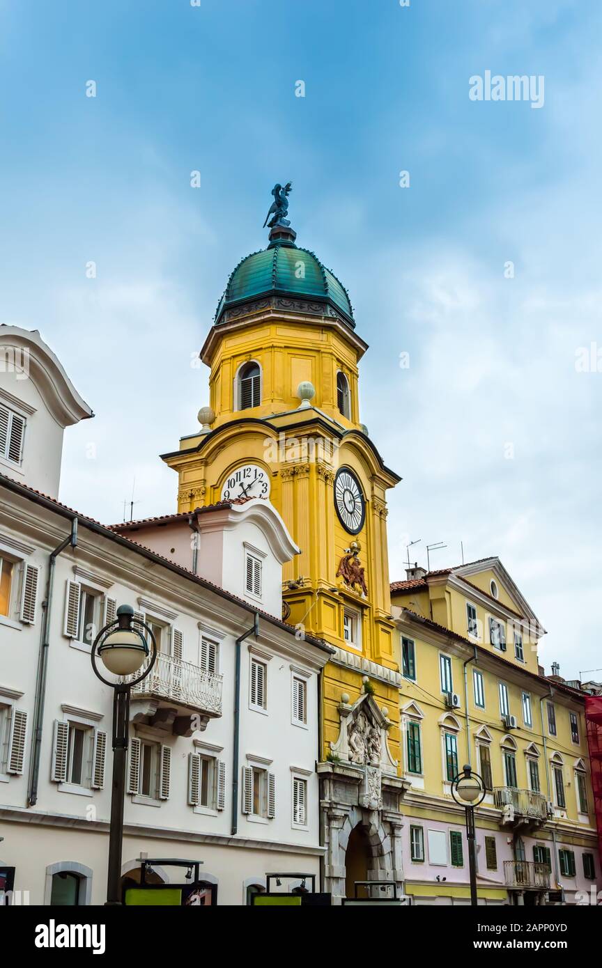 Torre dell'orologio della città barocca dipinta in giallo in una giornata di sole. Colorati vecchi edifici con file di finestre nel centro di Rijeka, Croazia Foto Stock