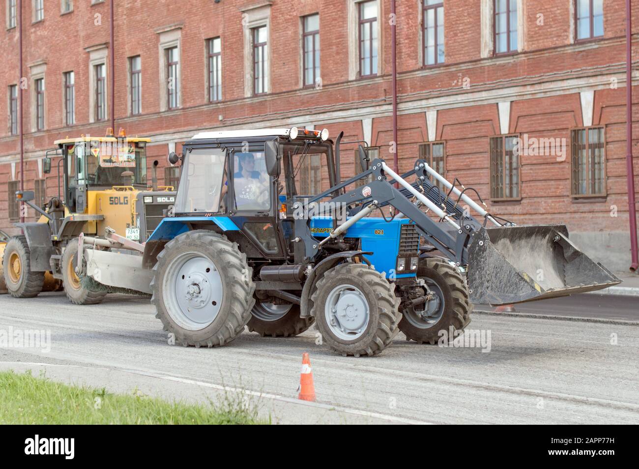 Trattore leggero bielorusso con ugello, benna e martello pneumatico, per la riparazione e la modernizzazione della strada asfaltata. Russia. Foto Stock