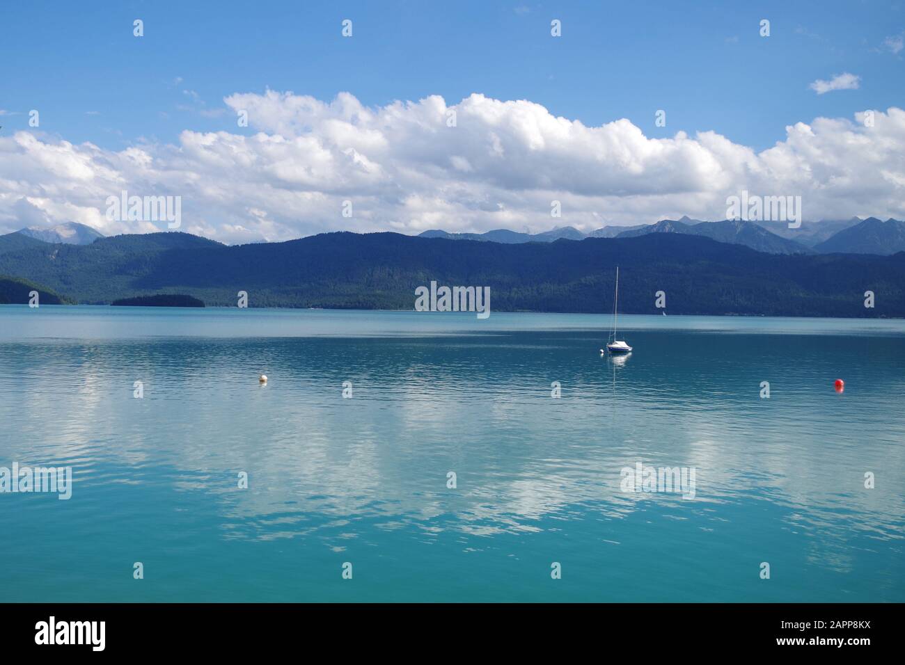 Un bellissimo lago blu con montagne boscose all'orizzonte in una soleggiata giornata estiva. Sull'acqua c'è una sola barca a vela. Foto Stock