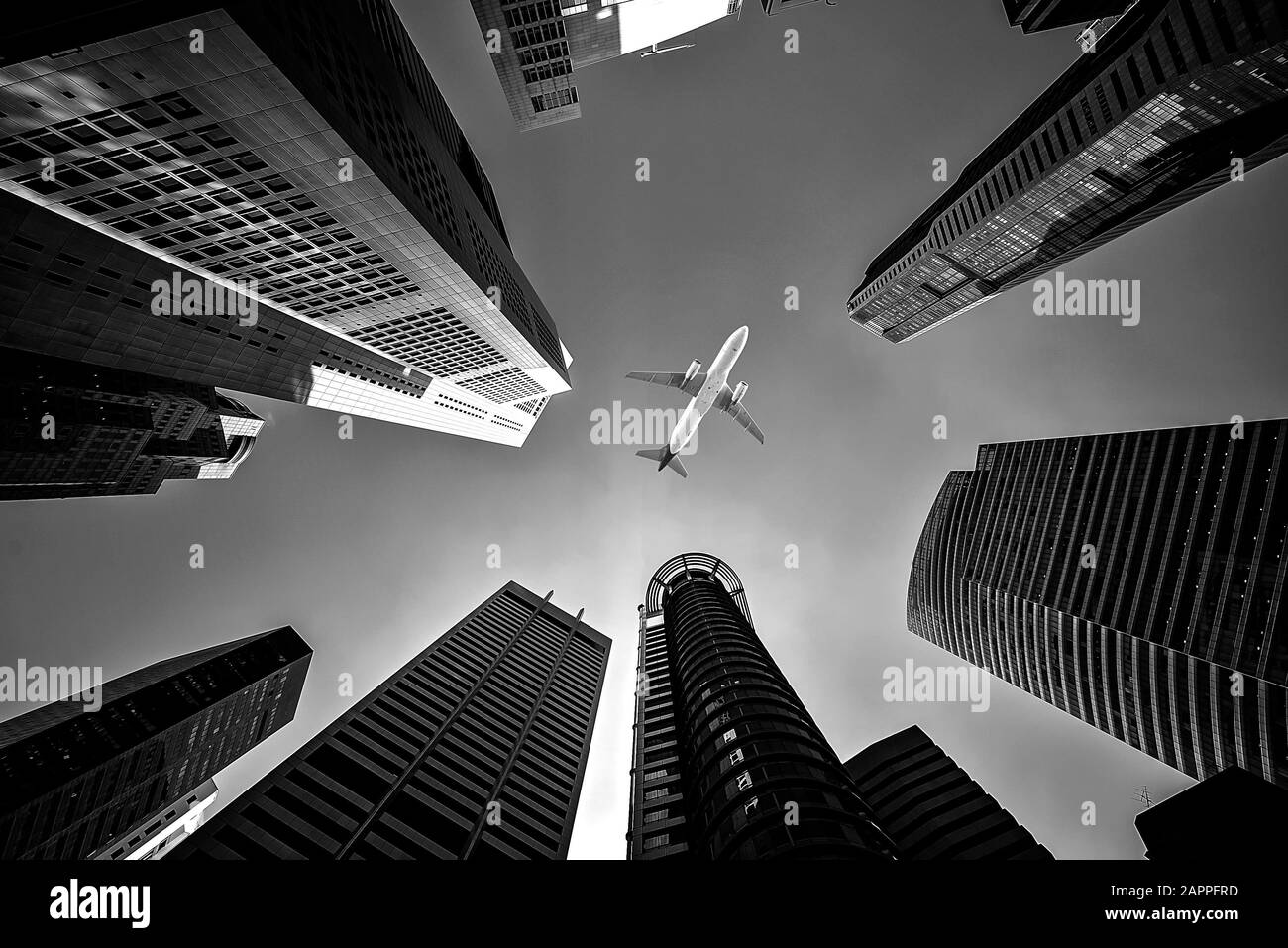 Alti edifici cittadini e un aereo che vola in alto, tono bianco e nero Foto Stock