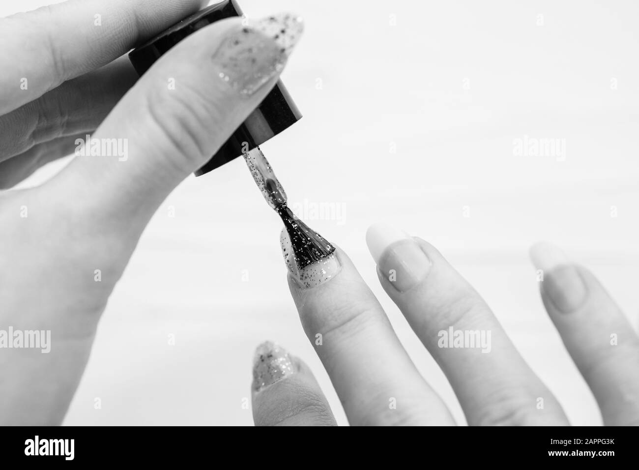 Mani femminili che fanno manicure, smalto per unghie in oro glitter colore su uno sfondo bianco. Concetto di salone di cura della pelle e del chiodo Foto Stock