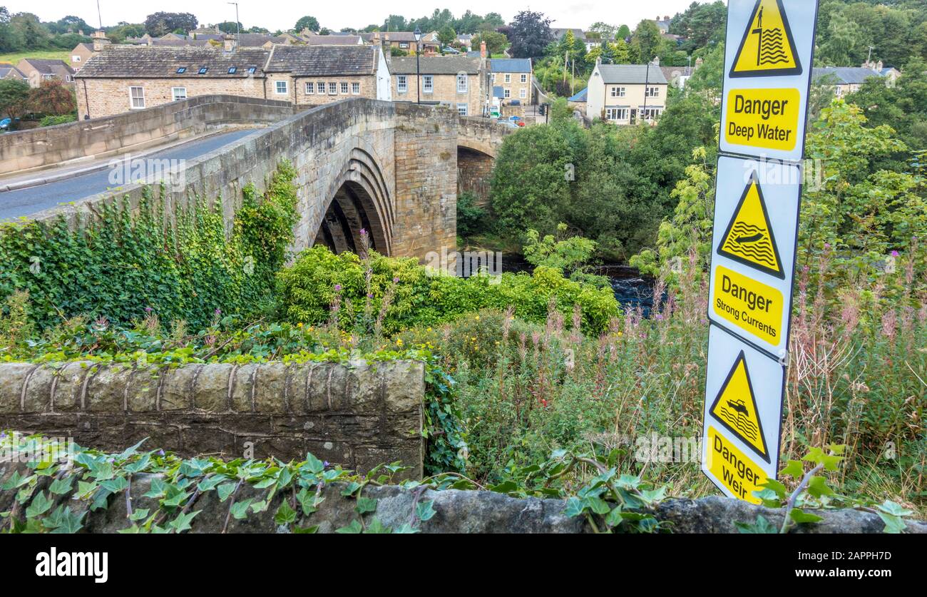 Ponte sul fiume Tees e un cartello sui pericoli di acque profonde, forti correnti e uno stramone. Barnard Castle, County Durham, Inghilterra, Regno Unito. Foto Stock
