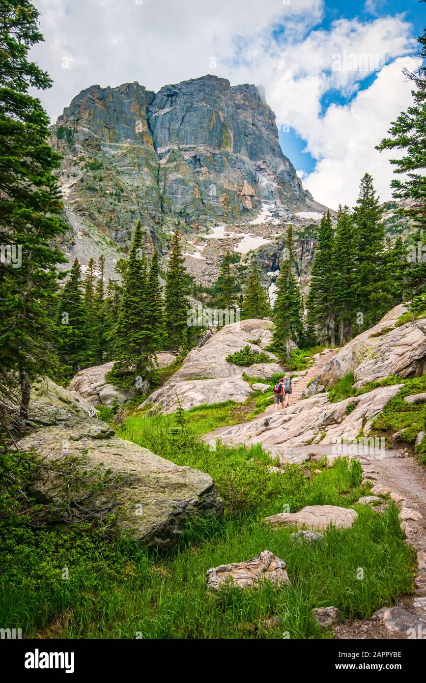 Un paio di escursionisti sul sentiero boscoso per Emerald Lake, Rocky Mountain National Park, CO. Cime di montagna con neve e nuvole a picco. Foto Stock