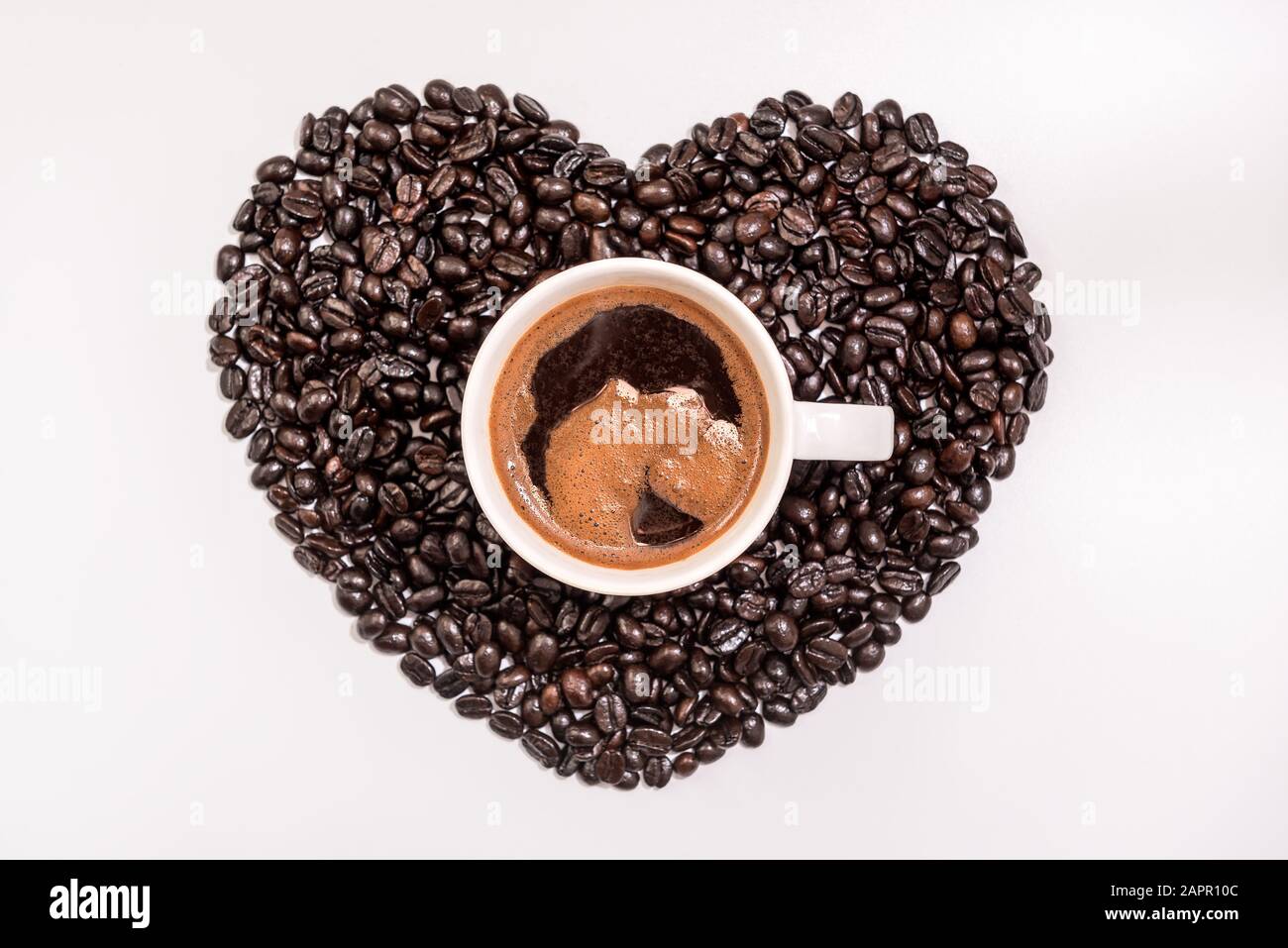 Vista dall'alto del gustoso caffè in tazza o tazza con cuore fatto di chicchi di caffè su sfondo bianco Foto Stock