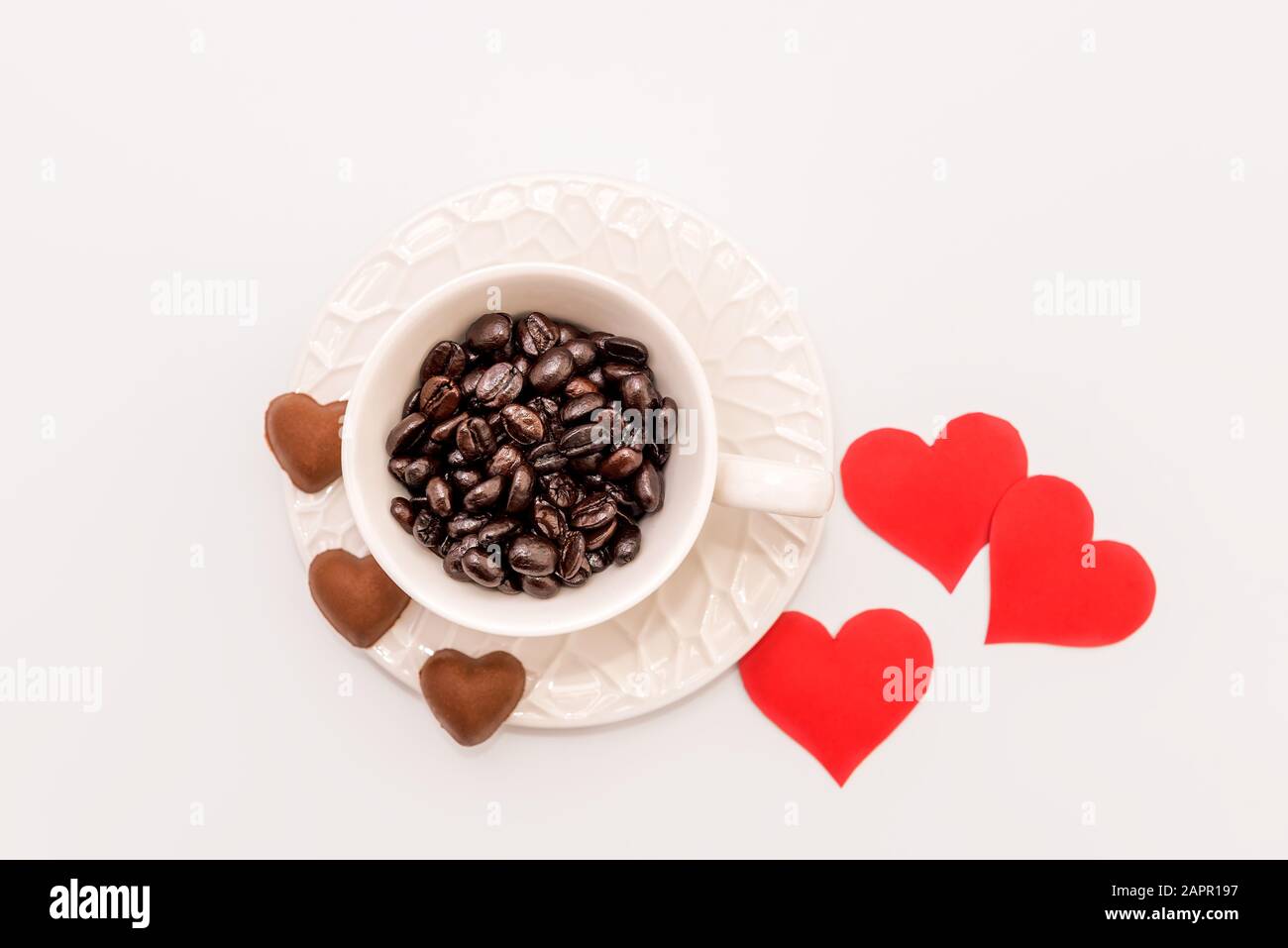 Vista dall'alto della tazza di caffè con biscotti al cioccolato a forma di cuore e cuori di carta rossa su sfondo bianco. Concetto di giorno di San Valentino Foto Stock