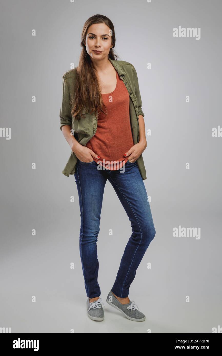 Bella giovane donna sorridente e in piedi su uno sfondo grigio Foto Stock