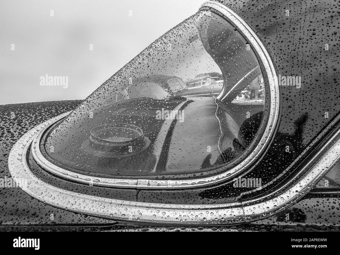 Immagine in scala di grigi della parte anteriore di un'auto coperta in gocce di pioggia Foto Stock