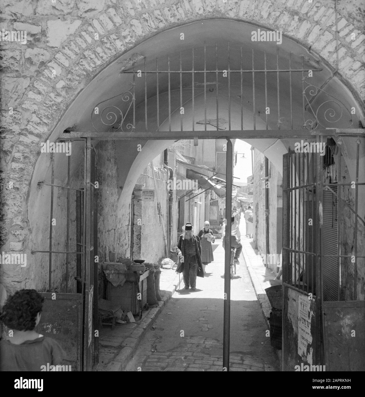 Israele 1964-1965: Gerusalemme (Gerusalemme), Mea Shearim Gateway attraverso la porta con attività quotidiana Annotazione: MEA Shearim, chiamato anche Meah Shearim o un centinaio di porte, è uno dei quartieri più antichi di Gerusalemme. Fu costruito a partire dal 1870 da ebrei asiatici che vivevano nella Città Vecchia fino ad allora. Tuttavia, c'era troppo poco spazio e così comprarono un pezzo di terra a nord-ovest della città. Questa terra, un'area paludata, fu coltivata in terra per costruire un nuovo quartiere: Meah Shearim. Il distretto è noto anno 2012 come il quartiere ebraico ortodosso più estremo del mondo ed è sede di diversi Hasi Foto Stock