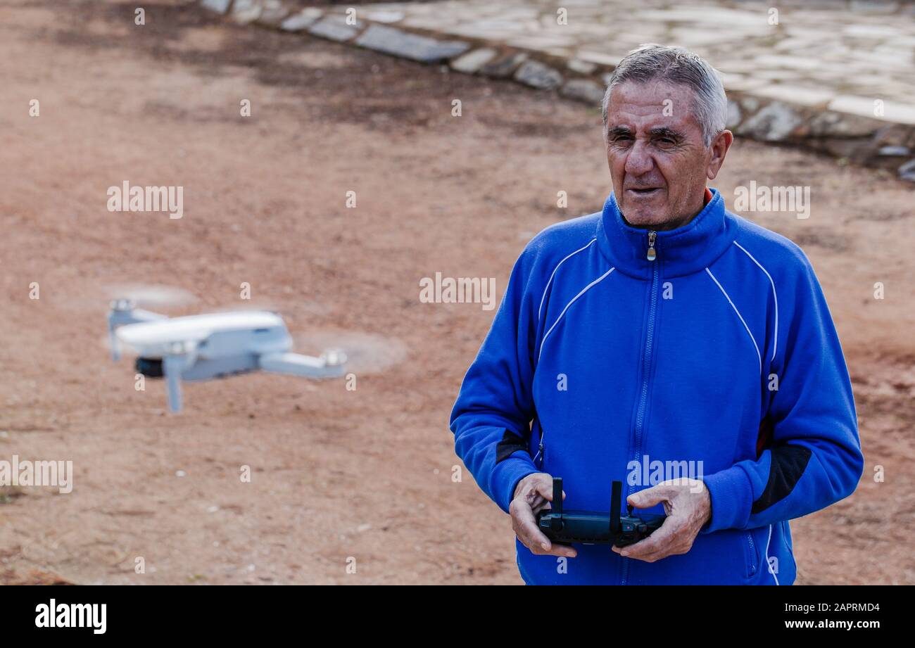 Vista laterale del vecchio uomo che vola il drone guardando il drone mentre in piedi contro gli alberi nel parco, concentrarsi sul vecchio uomo Foto Stock