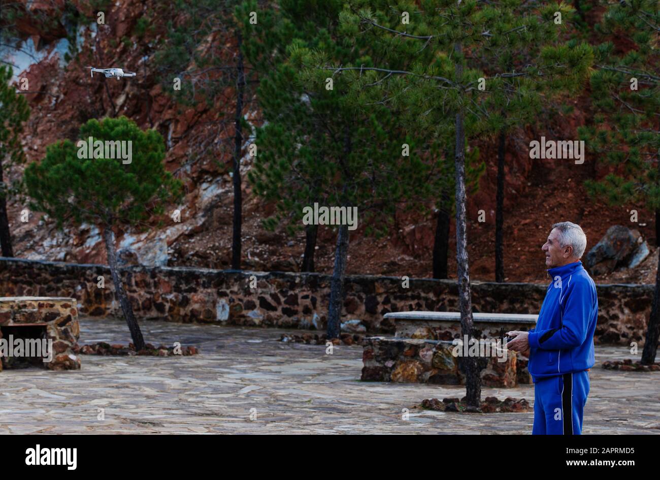 Vista laterale del vecchio uomo che vola il drone in abbigliamento sportivo mentre si trova contro gli alberi nel parco Foto Stock