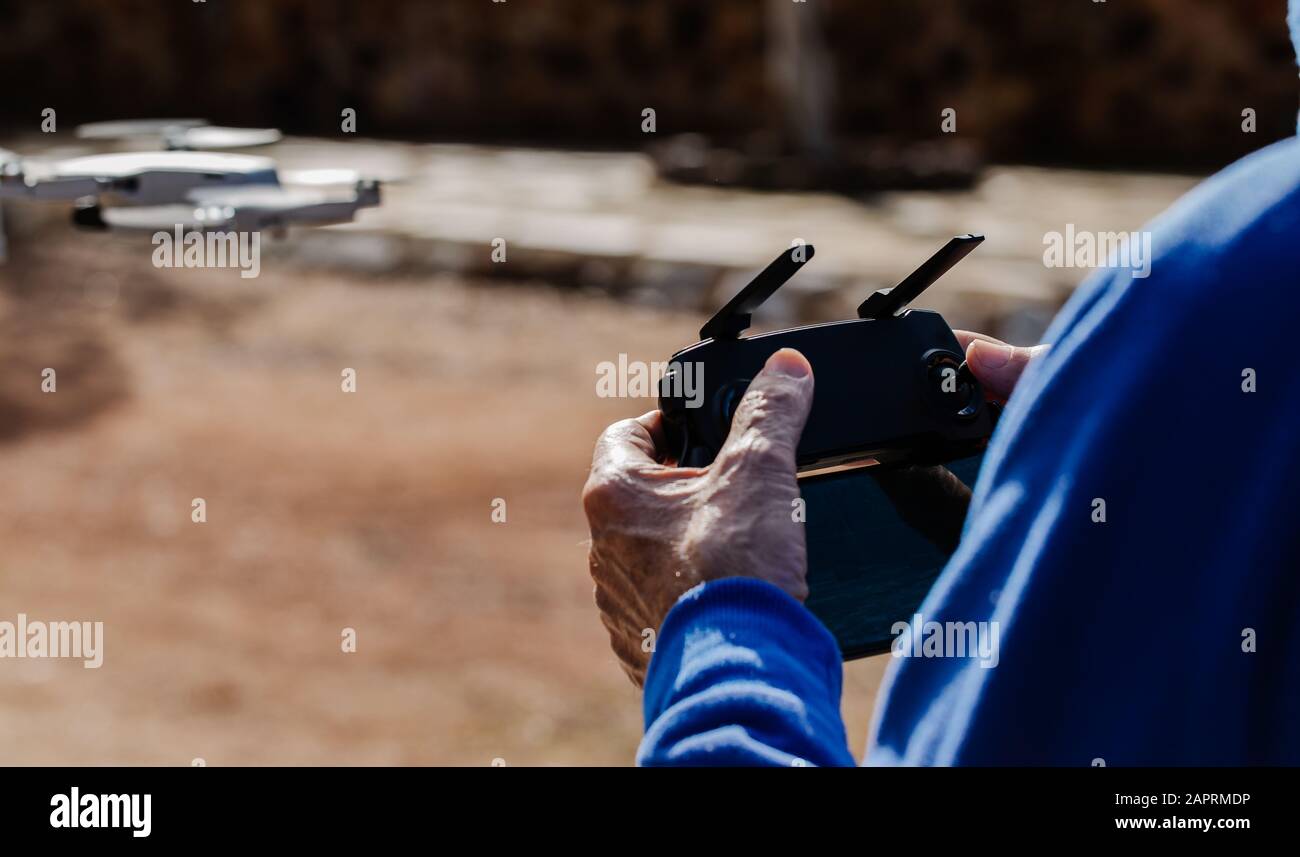 Vista posteriore dell'anziano che pilota il drone guardando il display del telecomando mentre è in piedi, messa a fuoco selettiva Foto Stock