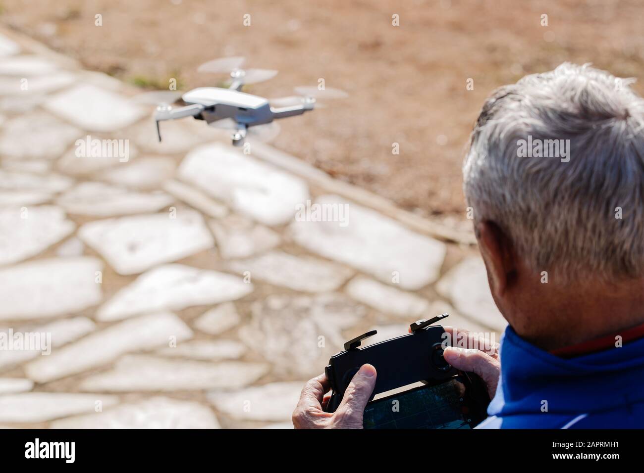 Vista posteriore dell'anziano che pilota il drone guardando il display del telecomando mentre è in piedi, messa a fuoco selettiva Foto Stock