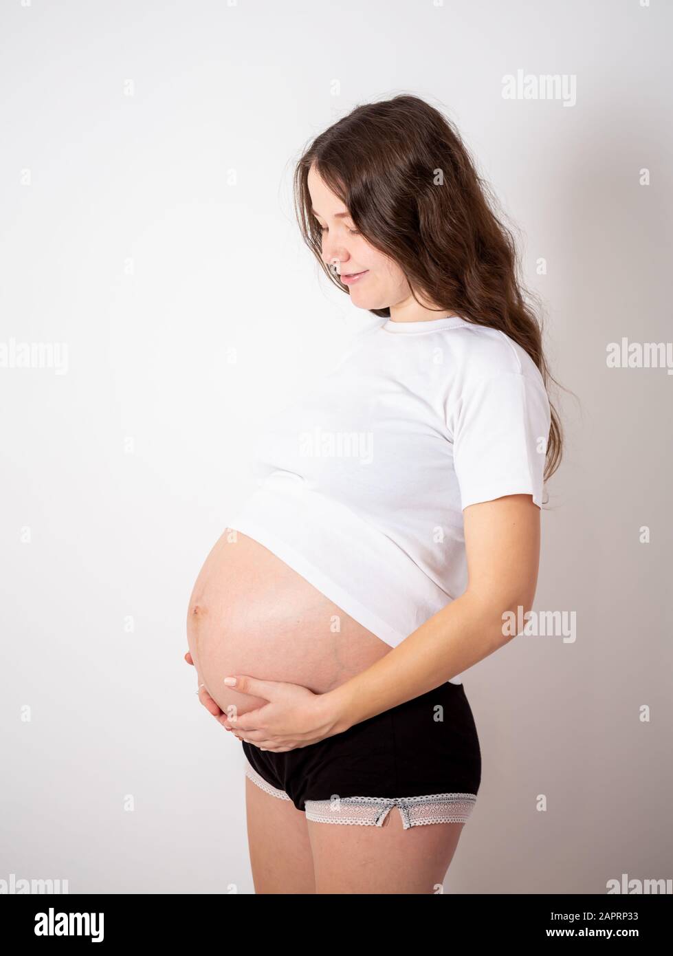 La giovane bella donna incinta sperimenta forti emozioni su uno sfondo bianco Foto Stock