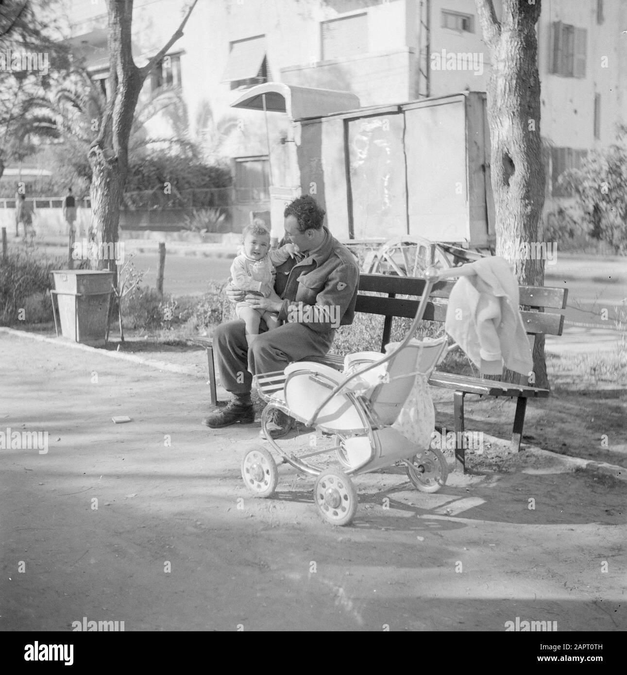 Israele 1948-1949: Tel Aviv un soldato in partenza su una panchina in un parco a Tel Aviv con il suo bambino in grembo e un passeggino Data: 1948 Località: Israele, Tel Aviv Parole Chiave: Famiglie, bambini, passeggini, soldati, parchi, sculture di strada, mobili di strada Foto Stock