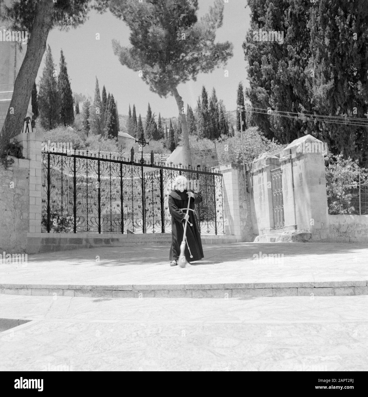 Israele 1964-1965. Ein-Karem Ein-Karim. Piazza vicino alla chiesa di O.L.Lady Visitation. In primo piano una recinzione in ferro battuto con una croce con le figure di Maria e Giovanni Ev. Un sacerdote francescano spazza il marciapiede Annotazione: Ein Karem, a sud-ovest di Gerusalemme, è un grazioso villaggio che è visitato principalmente da pellegrini cristiani e turisti perché Giovanni Battista è nato qui e vi ha vissuto con sua madre Elisabetta. Date: 1964 Location: Ein Karem, Israel Keywords: Francescani, recinzioni, edifici religiosi, monasteri Foto Stock