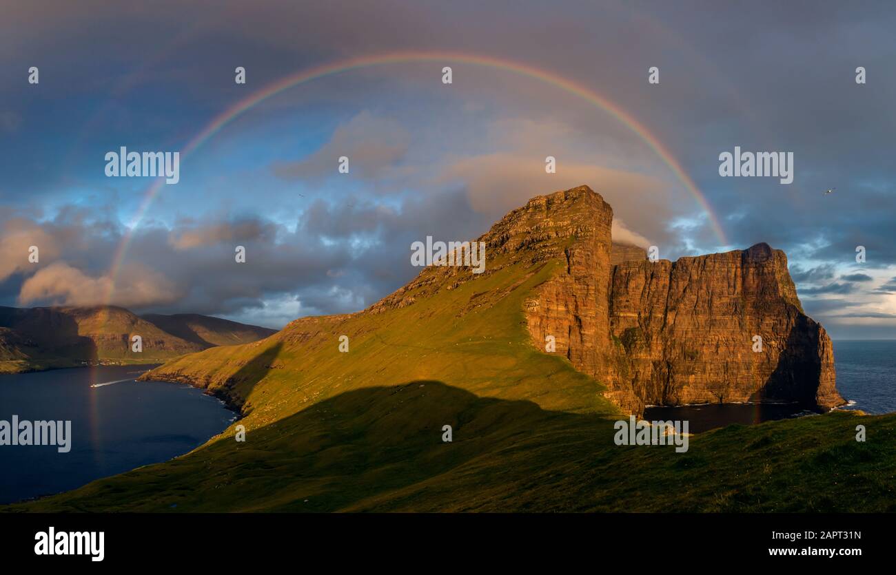 Un arcobaleno pieno al tramonto sulle scogliere dell'isola di Vagar. Isole Faroe Foto Stock