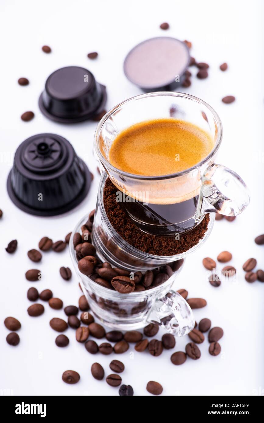 bicchieri di vetro, in sequenza verticale, con chicchi di caffè, macinato e cremoso espresso. Sullo sfondo alcune capsule di caffè Foto Stock