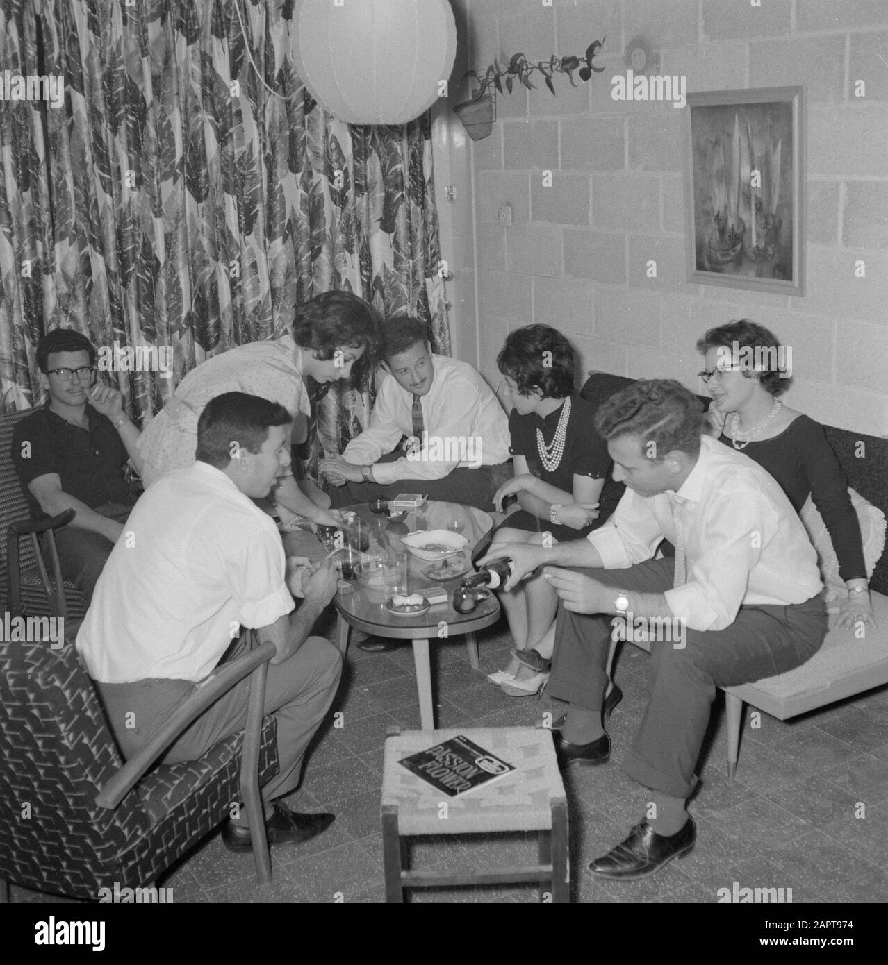 Gli ospiti di una festa in circolo domestico intorno al tavolo con uno spuntino e un drink. Capodanno. Data: 1 gennaio 1964 luogo: Israele Parole Chiave: Visite, feste, soggiorno, cibo, vino Foto Stock