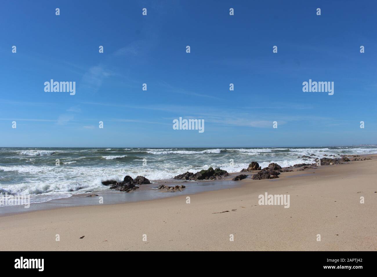Spiaggia di sabbia con alcune rocce, mare ondulato e cielo blu Foto Stock