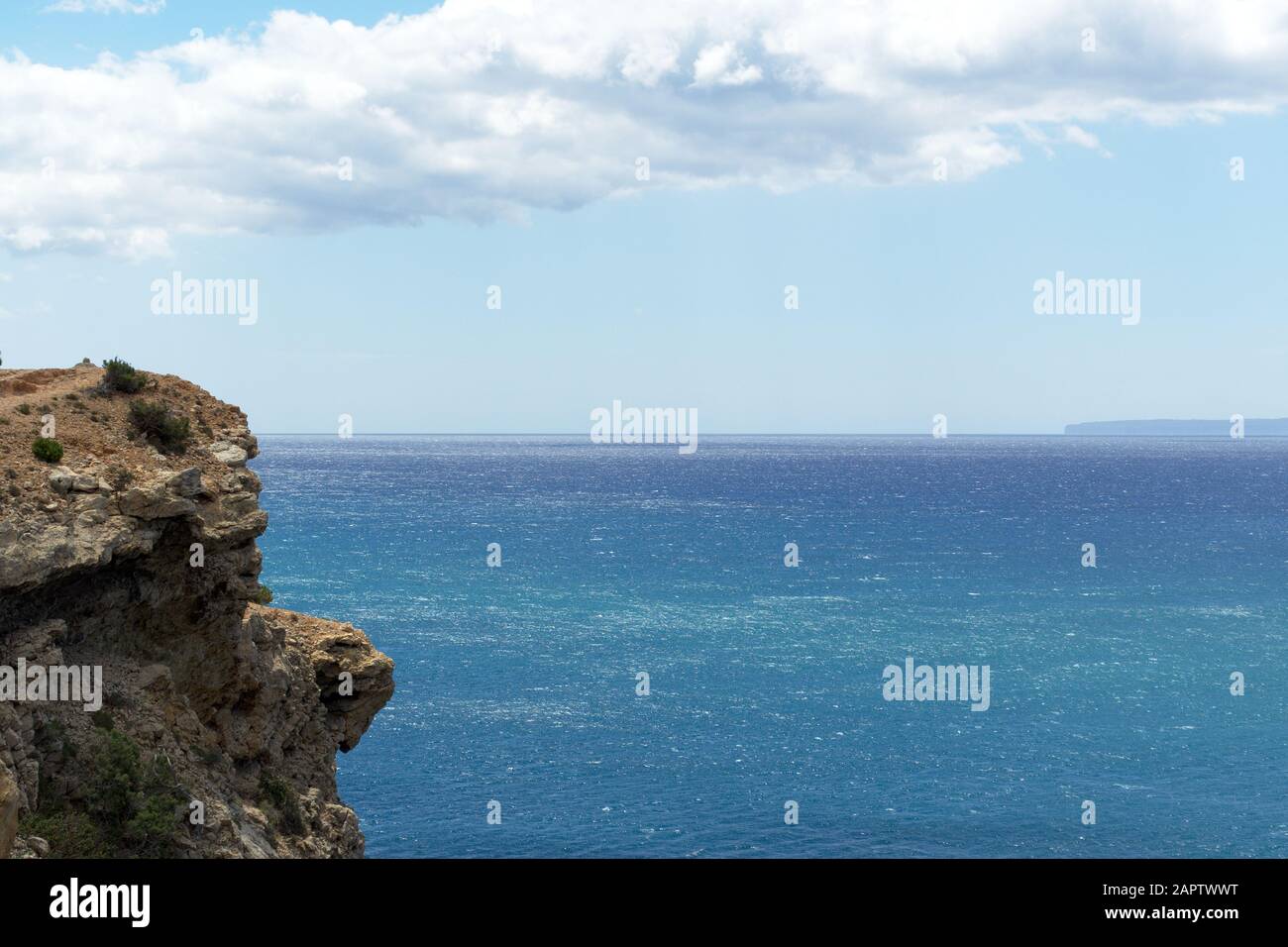 Costa rocciosa al mare delle Baleari con vegetazione, acqua blu e cielo nuvoloso. Isola di Ibiza, Spagna Foto Stock