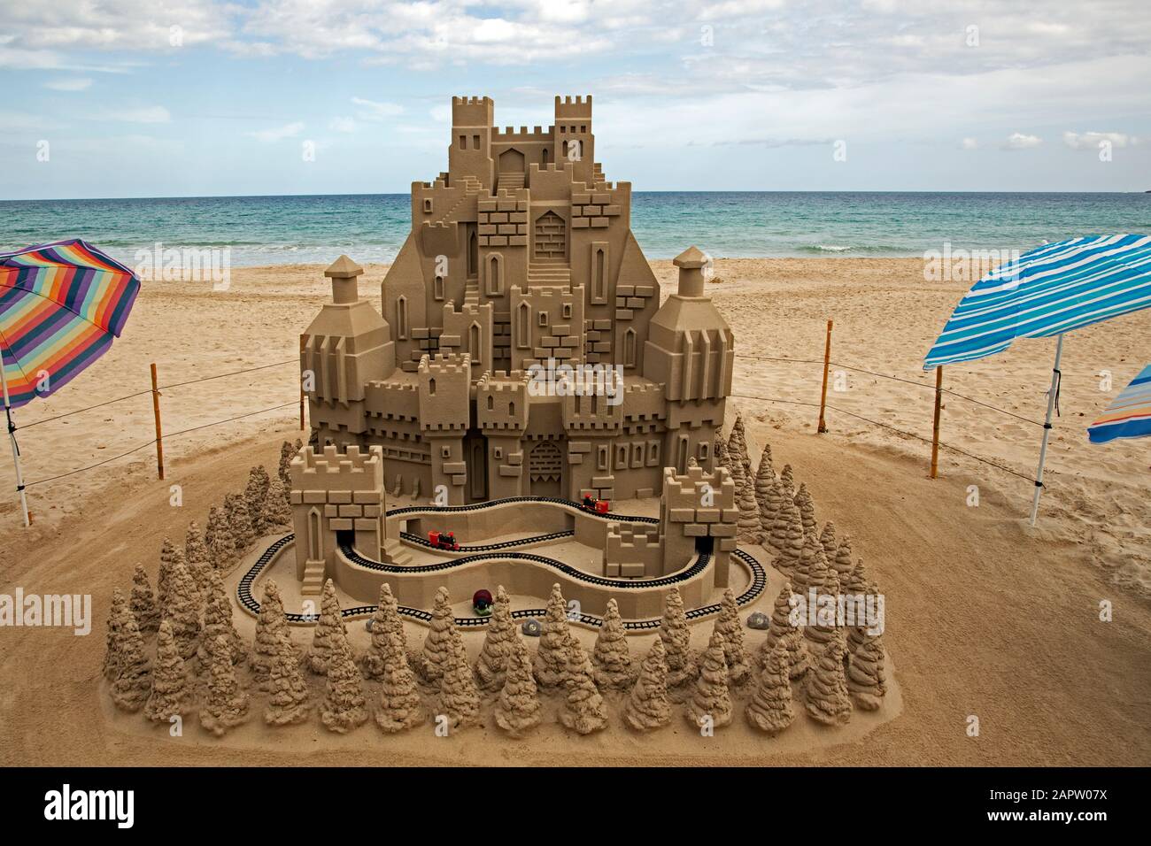 Un modellino ferroviario corre intorno ad un gigantesco castello di sabbia sulla spiaggia di Cala Millor, Maiorca, Spagna. Foto Stock