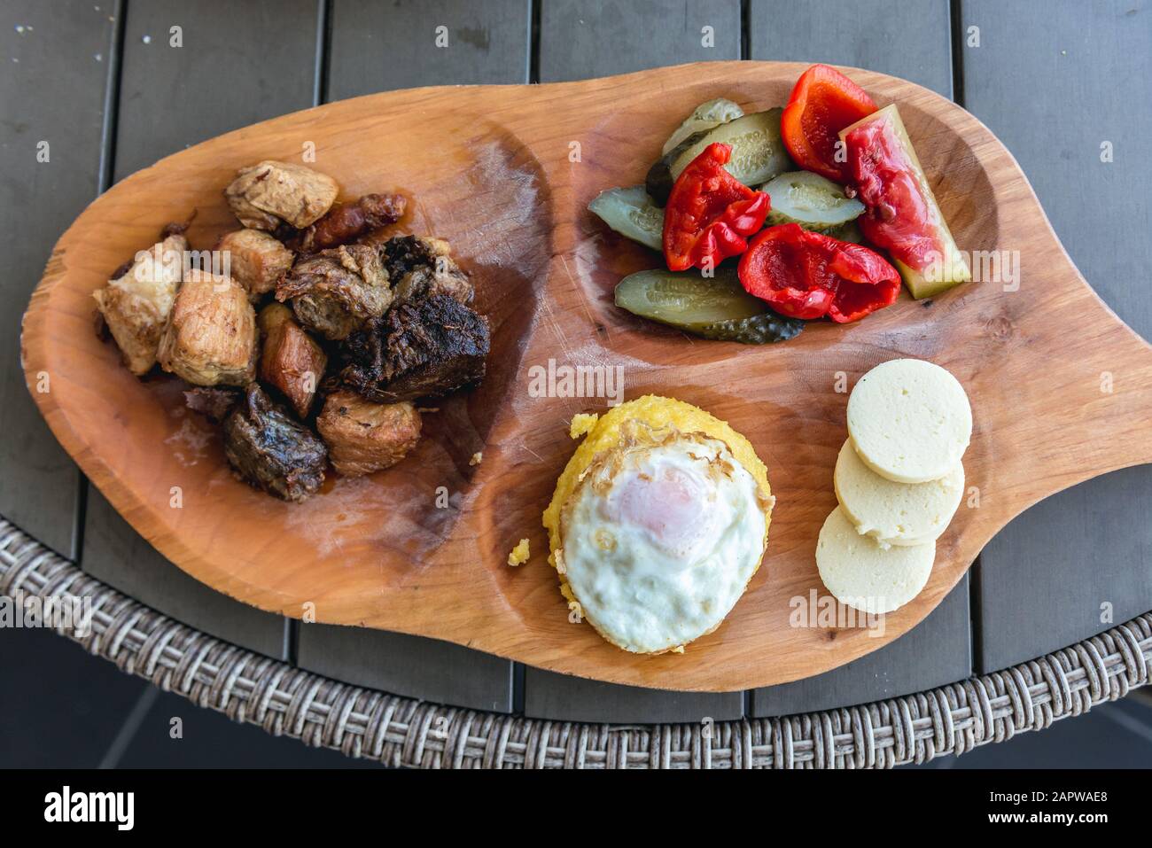 Piatto servito in ristorante rumeno - pezzi di carne con formaggio; cetrioli e uova fritte su mammaliga Foto Stock