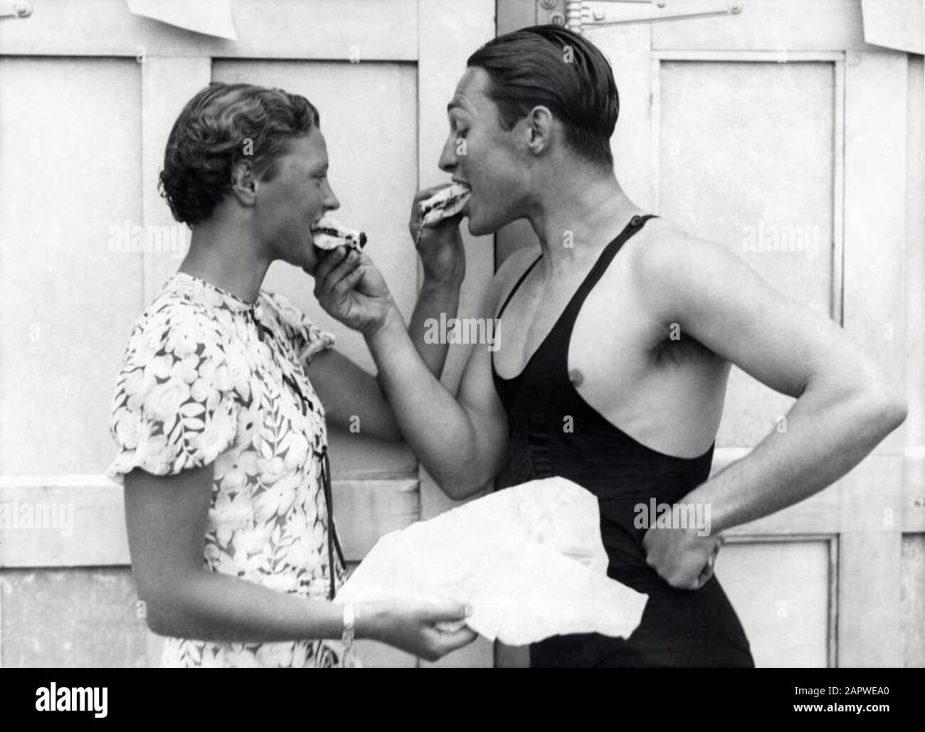 004000766 uomo in costume da bagno e giovane donna (nuotatore Willy den  Ouden) si danno un morso di bun. Inizio '30s, luogo sconosciuto. Uomo in  costume da bagno e donna che condividono