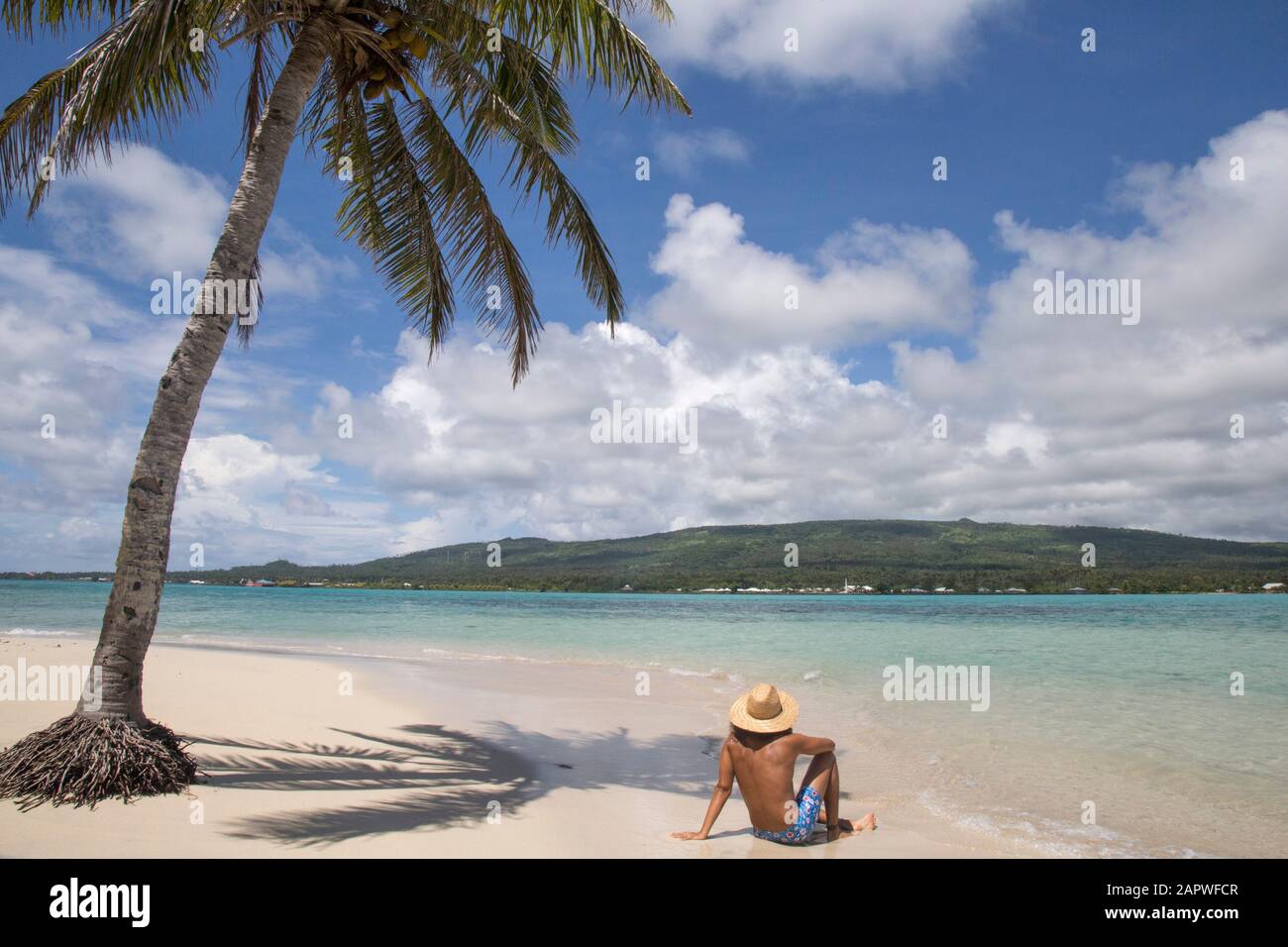 Un uomo, indossando costumi da bagno blu, sotto la palma sulla spiaggia di sabbia bianca Foto Stock