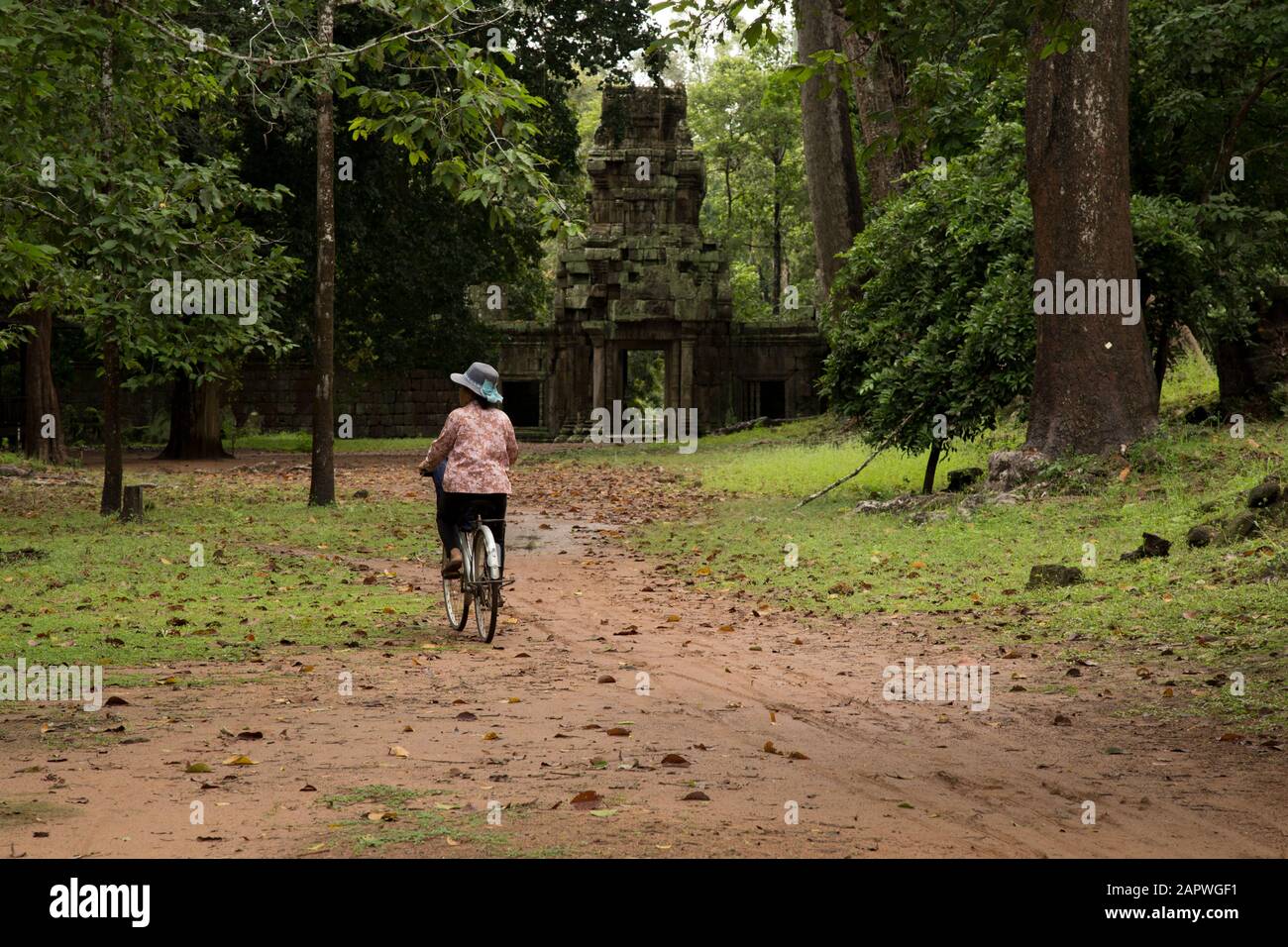Una donna che indossa un cappello, in bicicletta intorno alle vecchie rovine di Angkor Foto Stock