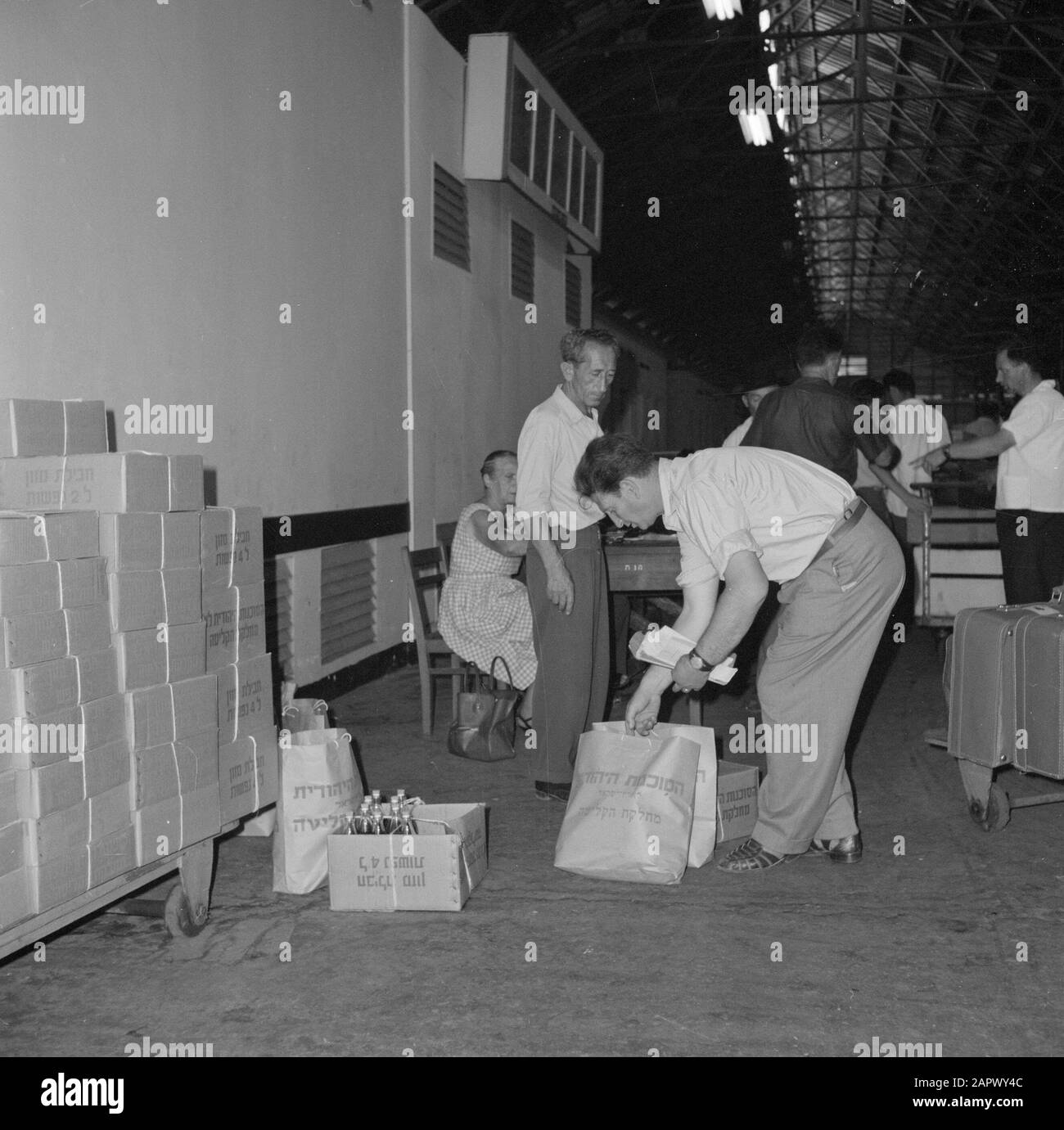 Israele 1964-1965: Haifa, arrivo di navi passeggeri; pacchetti doganali di cibo e bevande in dogana, anche i viaggiatori in attesa di valigie al Dogana Annotazione: Haifa è una città portuale e stazione balneare nel nord di Israele, nella parte più settentrionale delle montagne del Carmelo e sul Mar Mediterraneo. Nel 1945, ZIM Lines (compagnia di navigazione) iniziò come mittente di immigrati ebrei nel nuovo stato di Israele ed è diventata una delle più grandi compagnie di navigazione del mondo con filiali in tutto il mondo Data: 1964 Località: Haifa, Israele Parole Chiave: Bagagli, bevande, porti, pacchetti alimentari, magazzini Foto Stock
