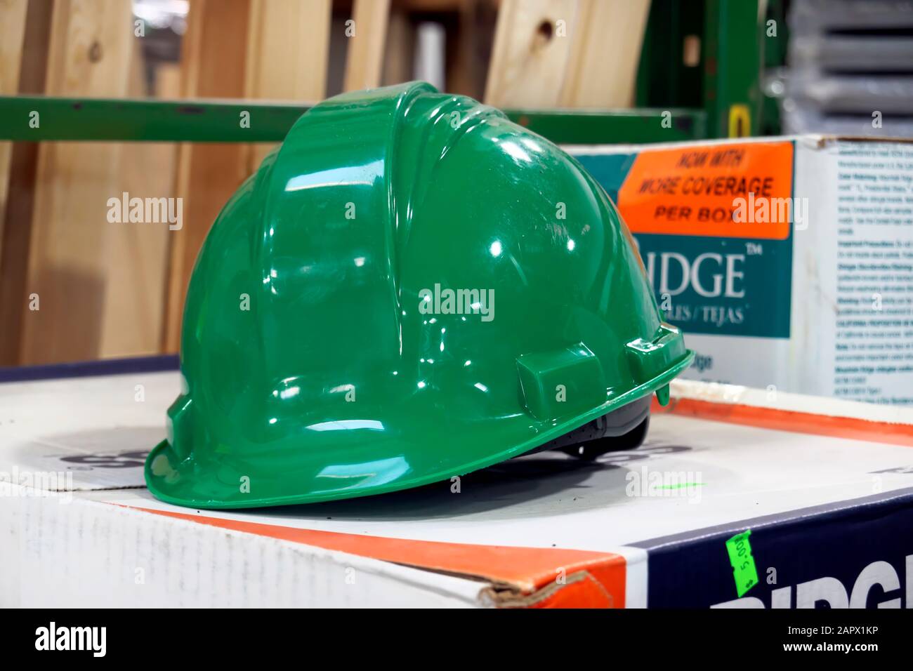 Un elmetto da costruzione verde appoggiato su una scatola di cartone all'interno di un negozio di ferramenta. Foto Stock