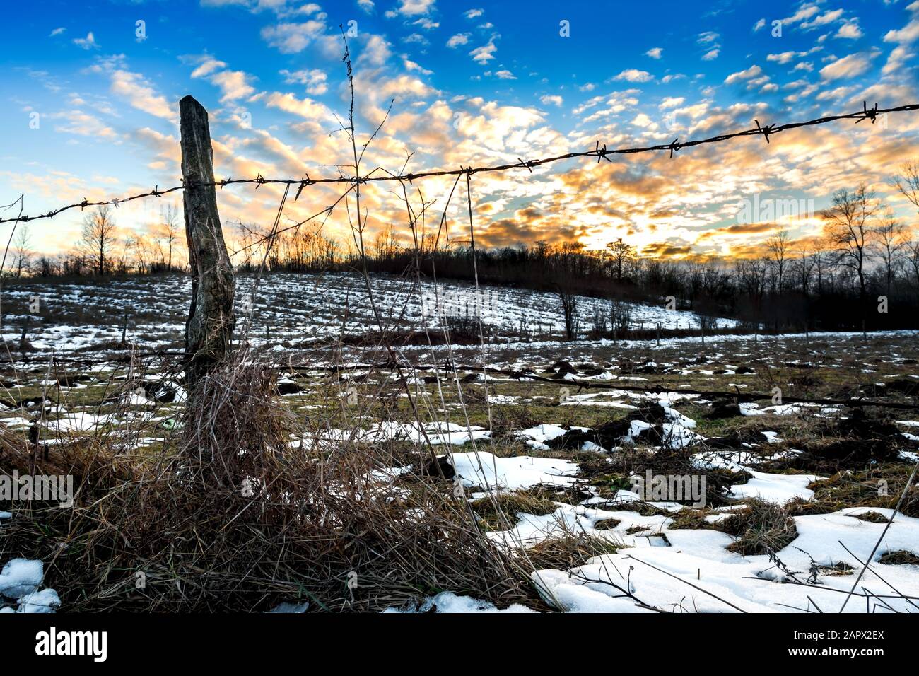 Splendido paesaggio invernale al tramonto con recinzione in filo spinato e cielo spettacolare. Foto Stock