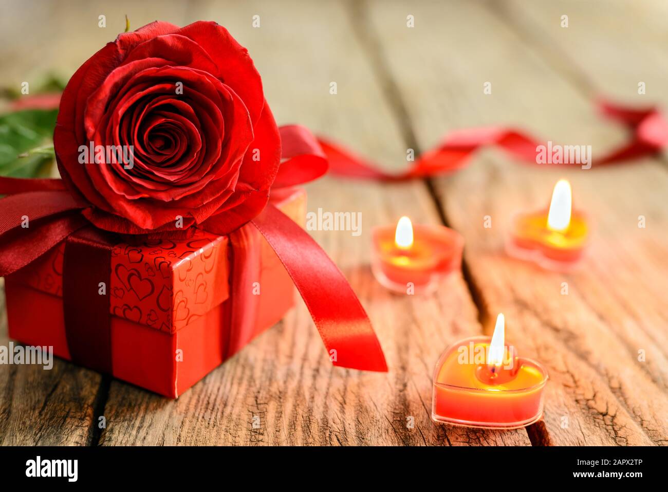 Concetto di giorno di San Valentino. Rosa rossa, scatola regalo e candele brucianti su vecchio tavolo di legno. Messa a fuoco selettiva. Foto Stock