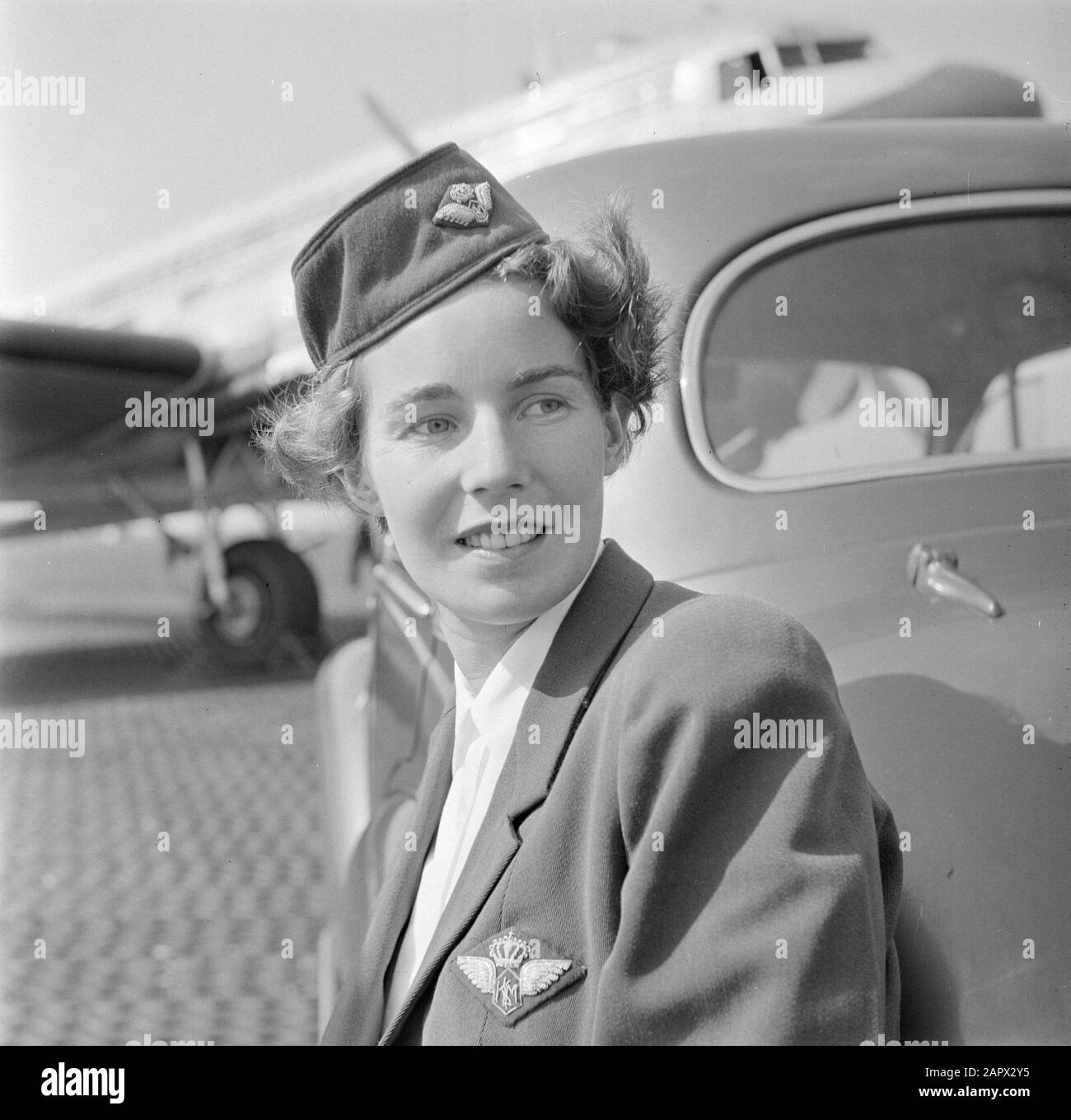 Identità aziendale del personale KLM e Schiphol Ritratto di una hostess KLM appoggiato su un'auto con Douglas DC-3 in background Data: Agosto 1951 Parole Chiave: Automobili, ritratti, assistenti di volo, aerei, personale aeronautico Foto Stock