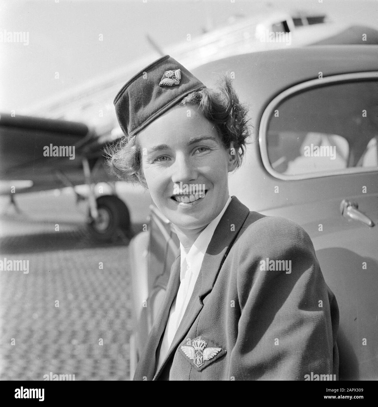 Identità aziendale del personale KLM e Schiphol Ritratto di una hostess KLM appoggiato su un'auto con Douglas DC-3 in background Data: Agosto 1951 Parole Chiave: Automobili, ritratti, assistenti di volo, aerei, personale aeronautico Foto Stock