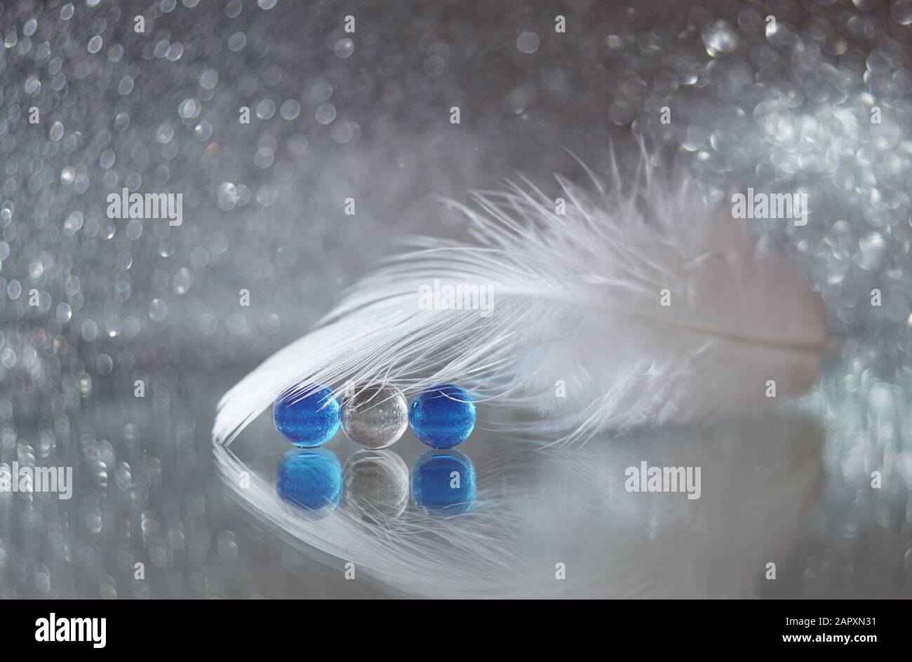 Una piuma bianca e bolle blu e bianche su uno specchio su uno sfondo argentato Foto Stock